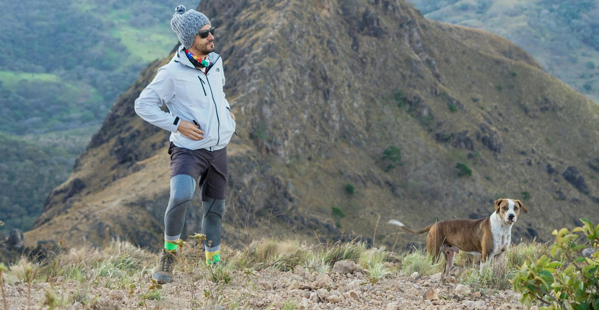 Man in hiking clothes and dog on a mountain peak.