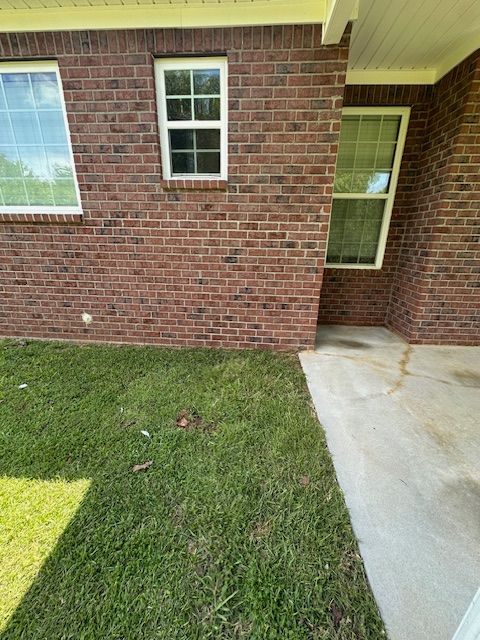 A brick house with two windows and a concrete walkway in front of it.