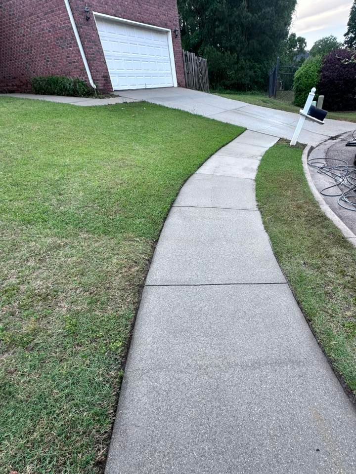 A concrete walkway leading to a brick house with a lush green lawn.