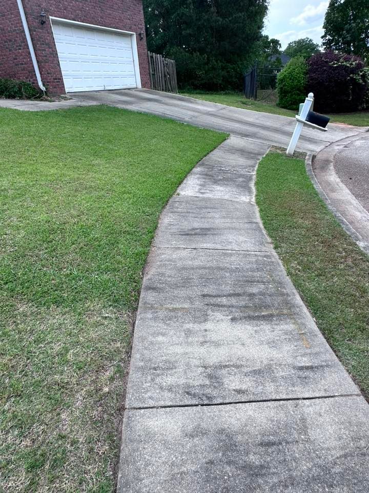 A concrete walkway leading to a house with a mailbox on the side of it.