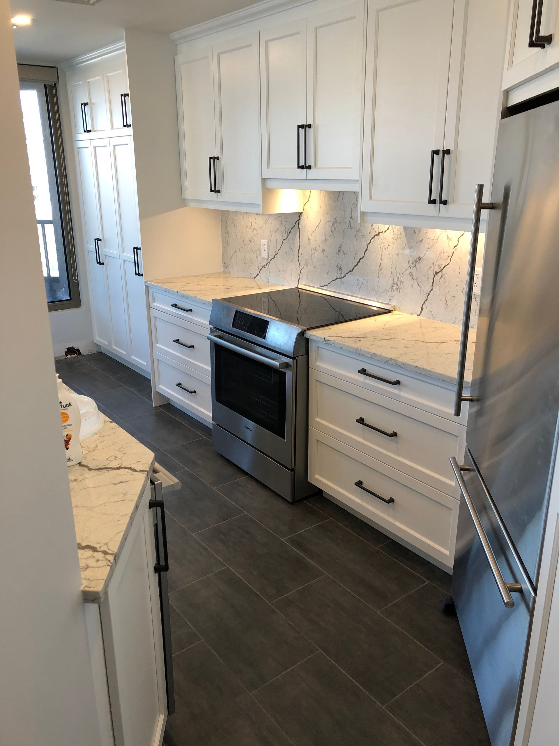 Une cuisine avec des armoires blanches, des appareils électroménagers en acier inoxydable et des comptoirs en marbre.