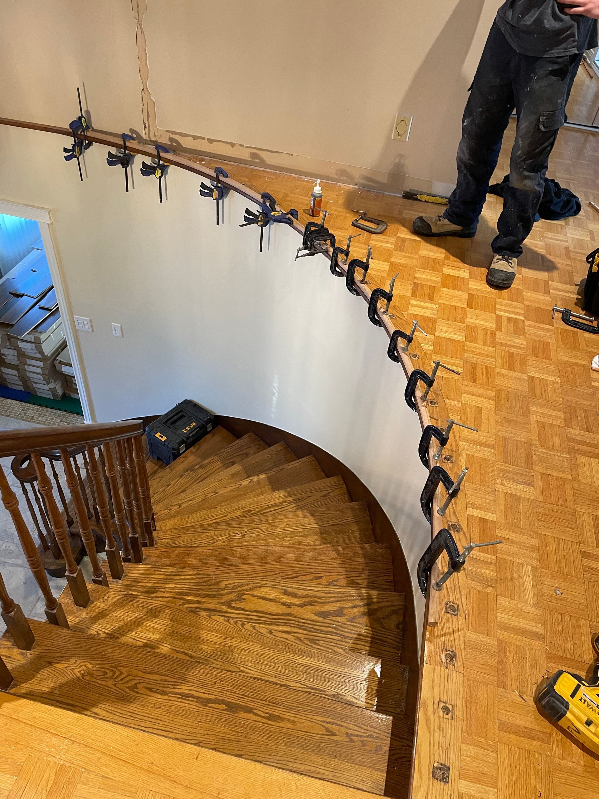 Un homme est debout sur un parquet à côté d'un escalier courbe.