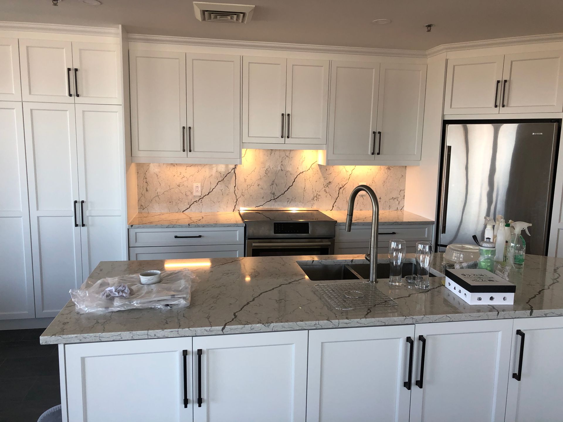 Une cuisine avec armoires blanches, comptoirs en granit, électroménagers en acier inoxydable et un grand îlot.