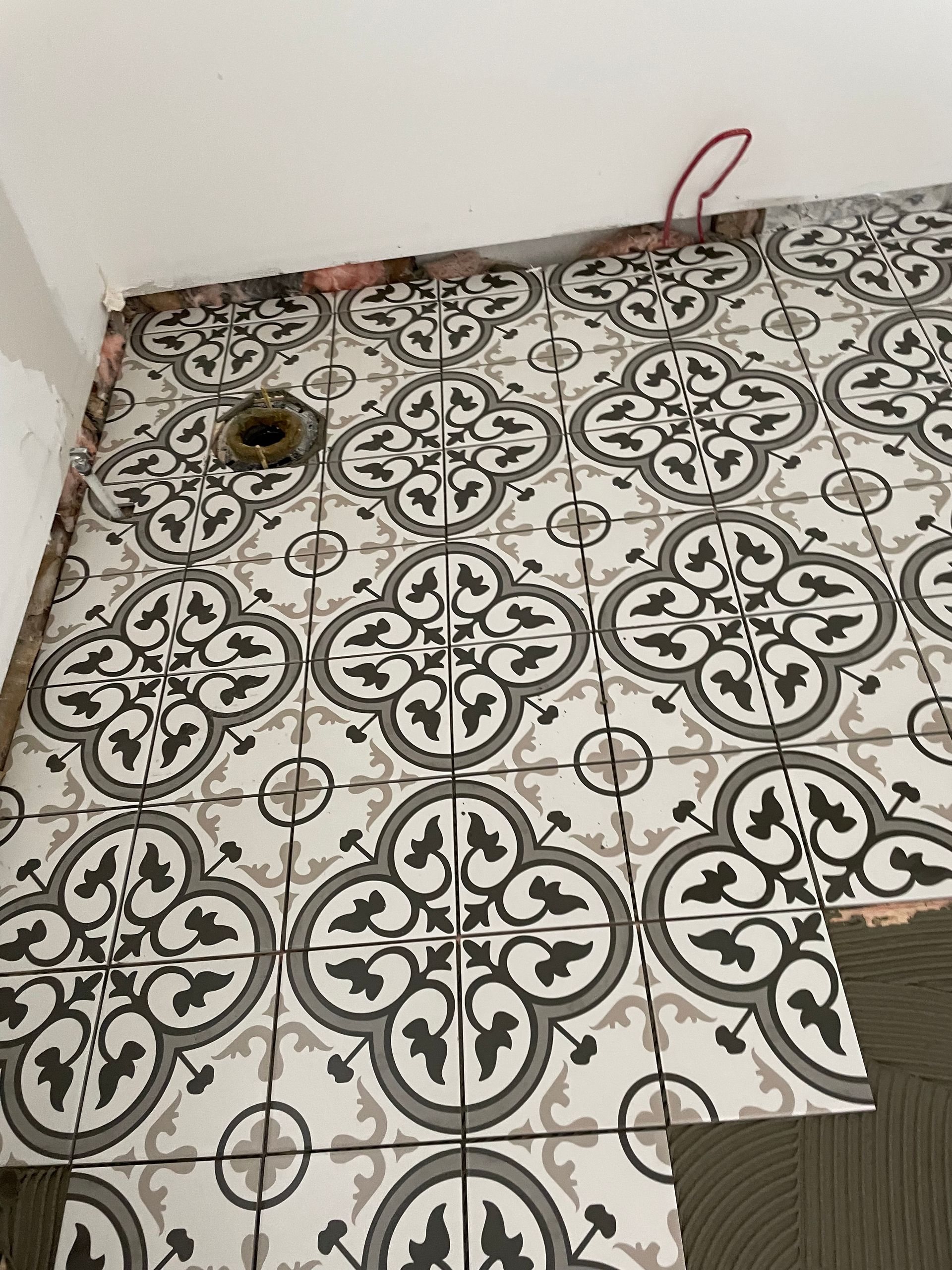 Un sol carrelé à motif floral est en cours de pose dans une salle de bain.