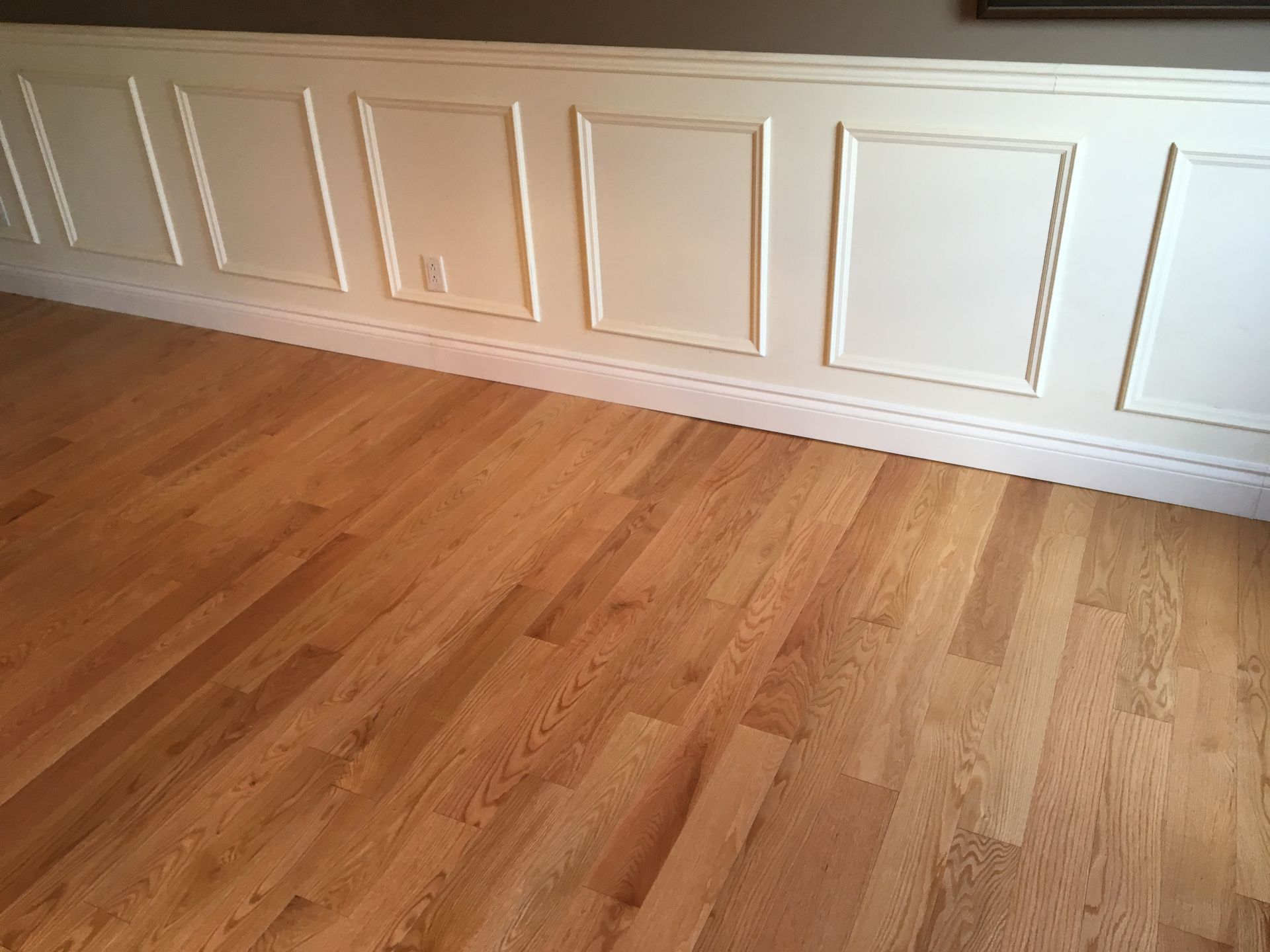 Une pièce avec parquet et boiseries blanches sur les murs.