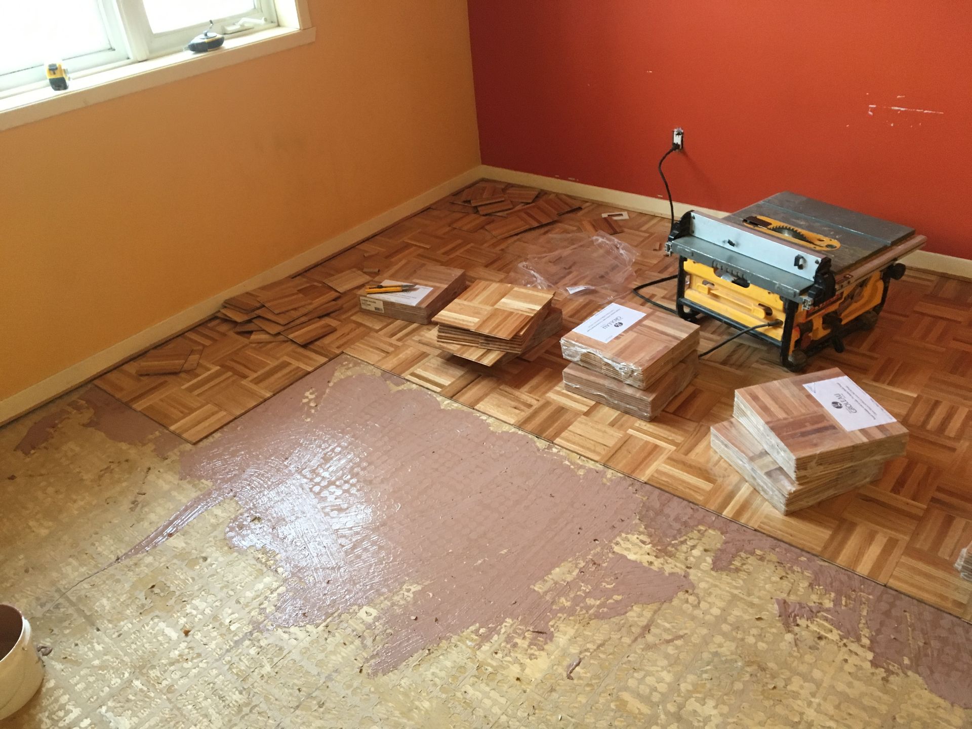 Une pièce avec un parquet en bois et une scie à table au sol.