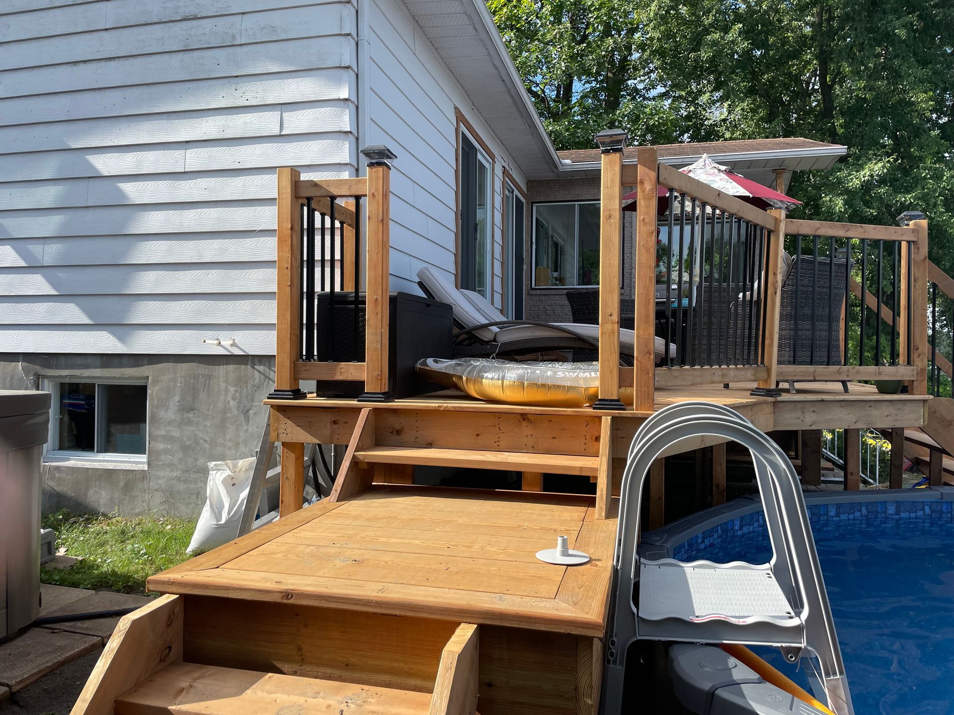 Une terrasse en bois avec escalier menant à une piscine à côté d'une maison.