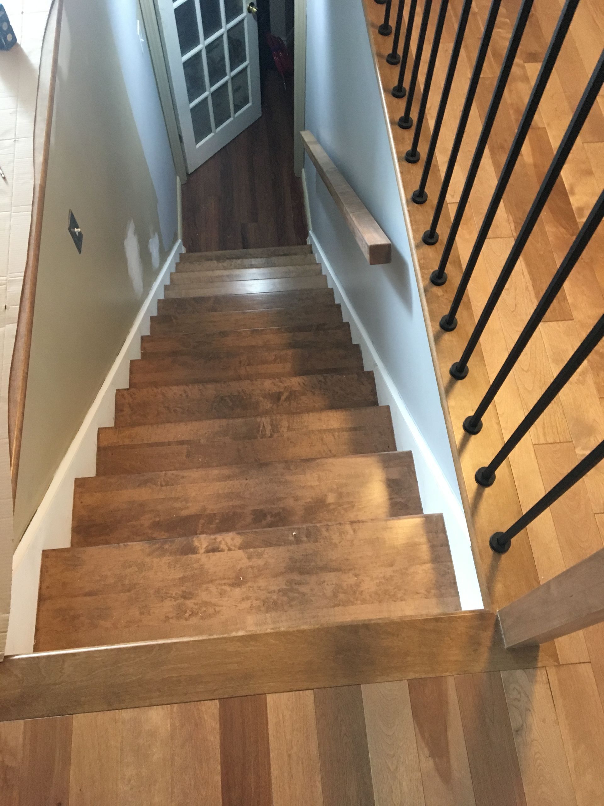 Un escalier en bois avec une rampe noire menant à une porte.