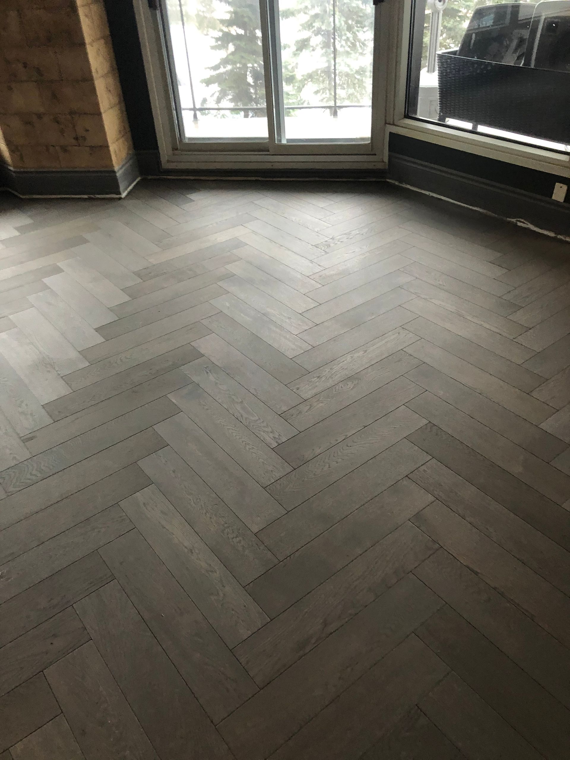 Une pièce avec un parquet à bâtons rompus et une grande fenêtre.