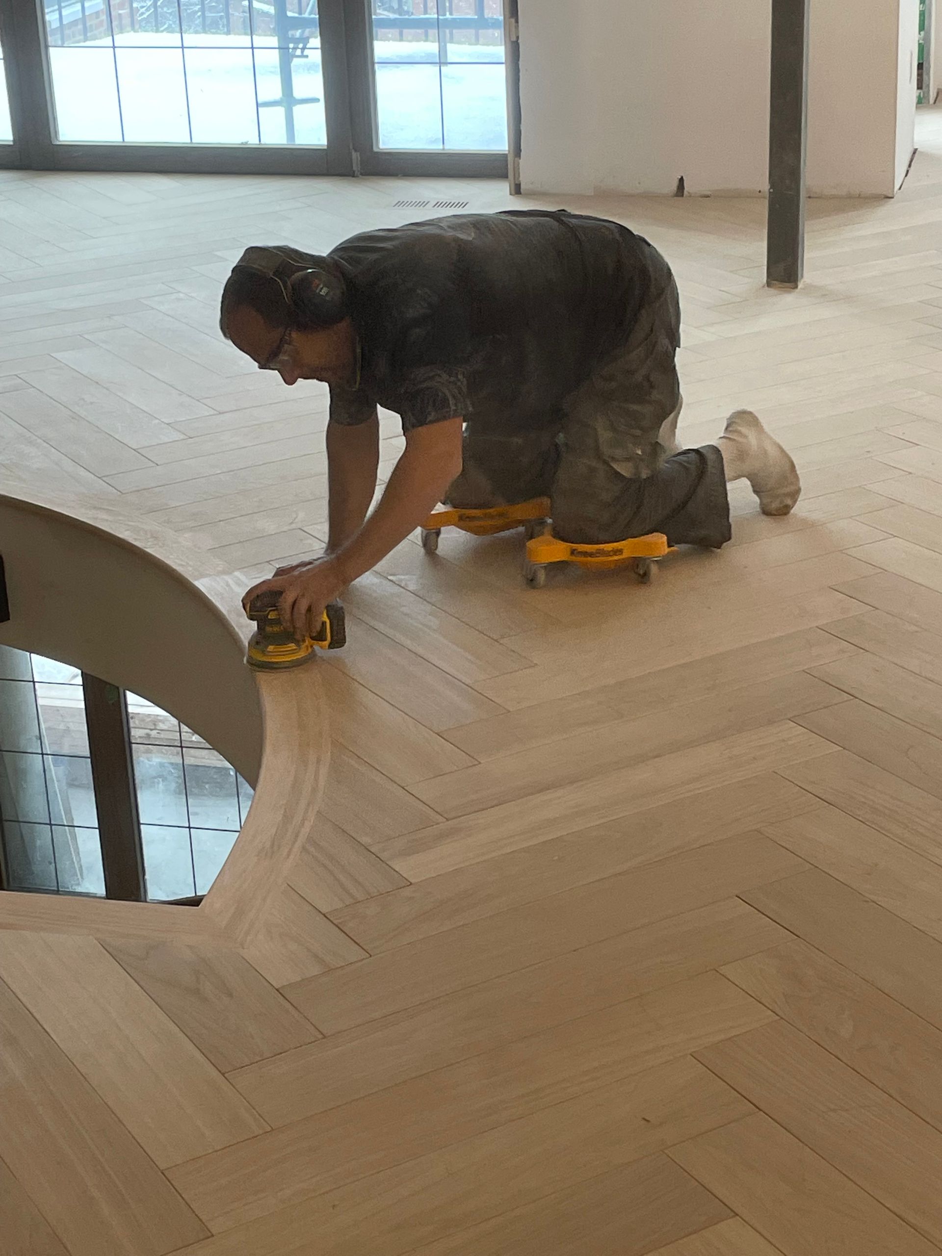 Un homme est agenouillé sur un plancher en bois en utilisant une ponceuse.