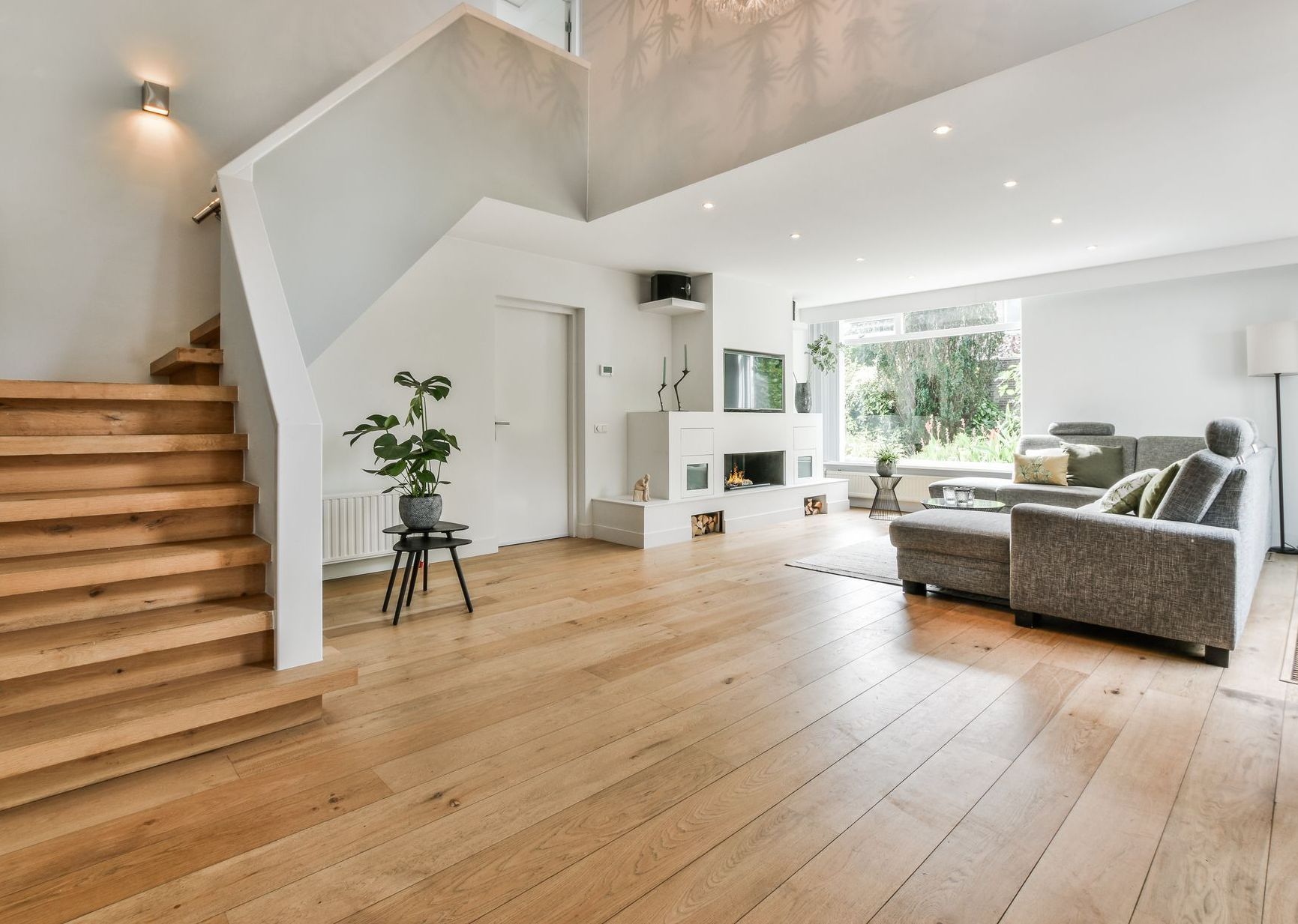 Un escalier en bois mène à un salon moderne avec une cheminée, un canapé et de grandes fenêtres.
