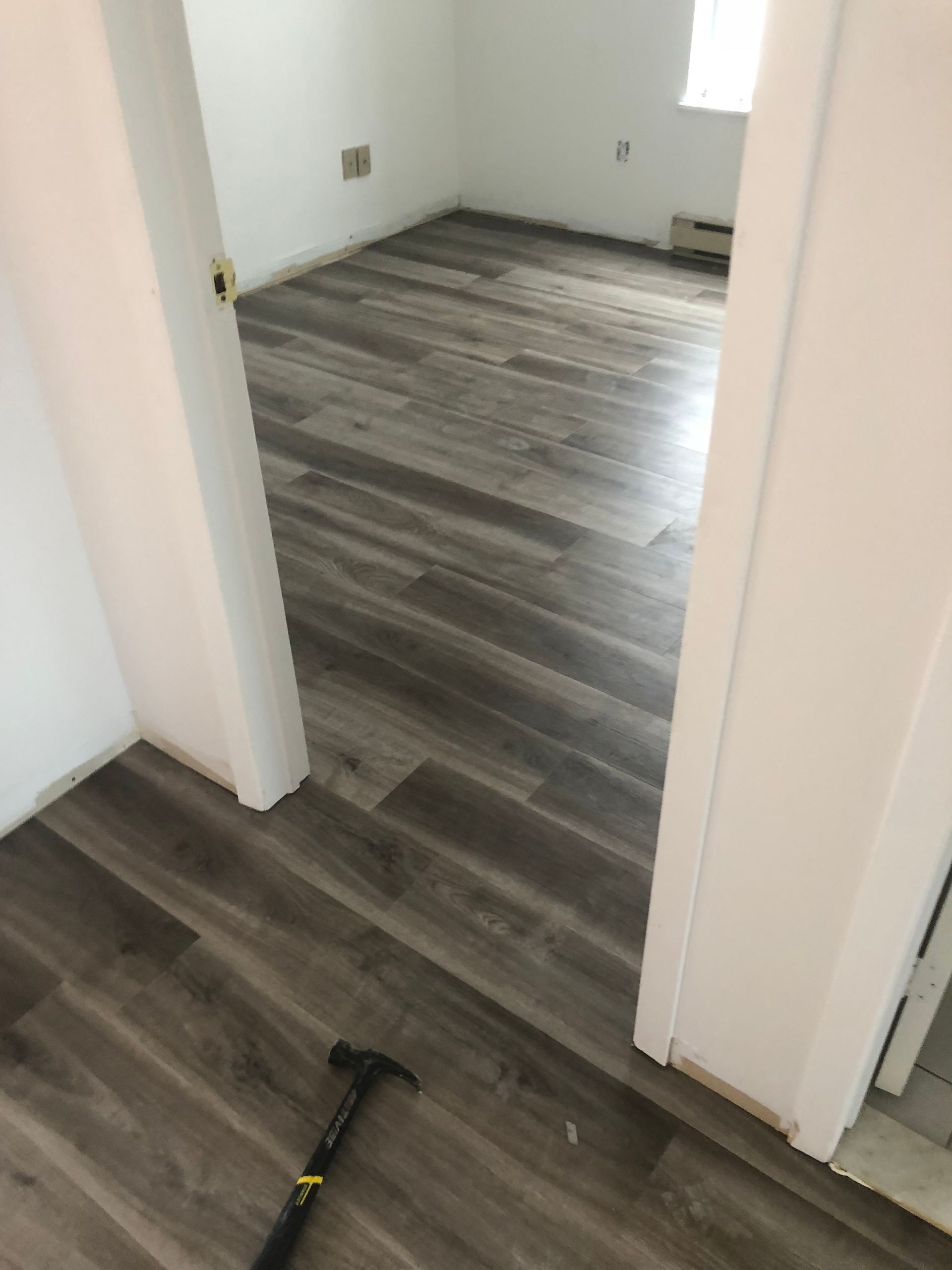 Une pièce avec du parquet et un marteau au sol.