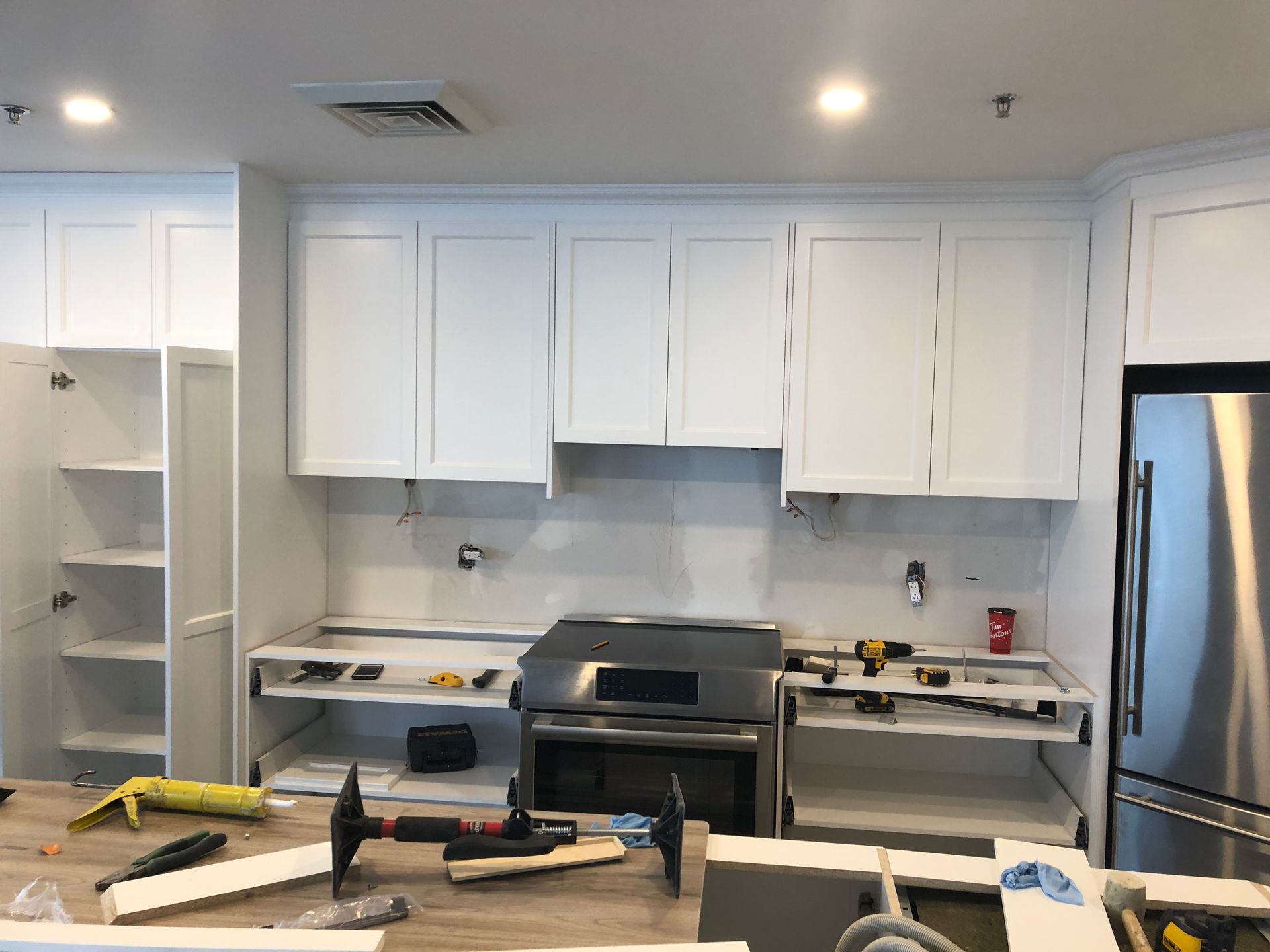 Cuisine en construction, armoires blanches, électroménagers en acier inoxydable, outils et matériaux sur les comptoirs.