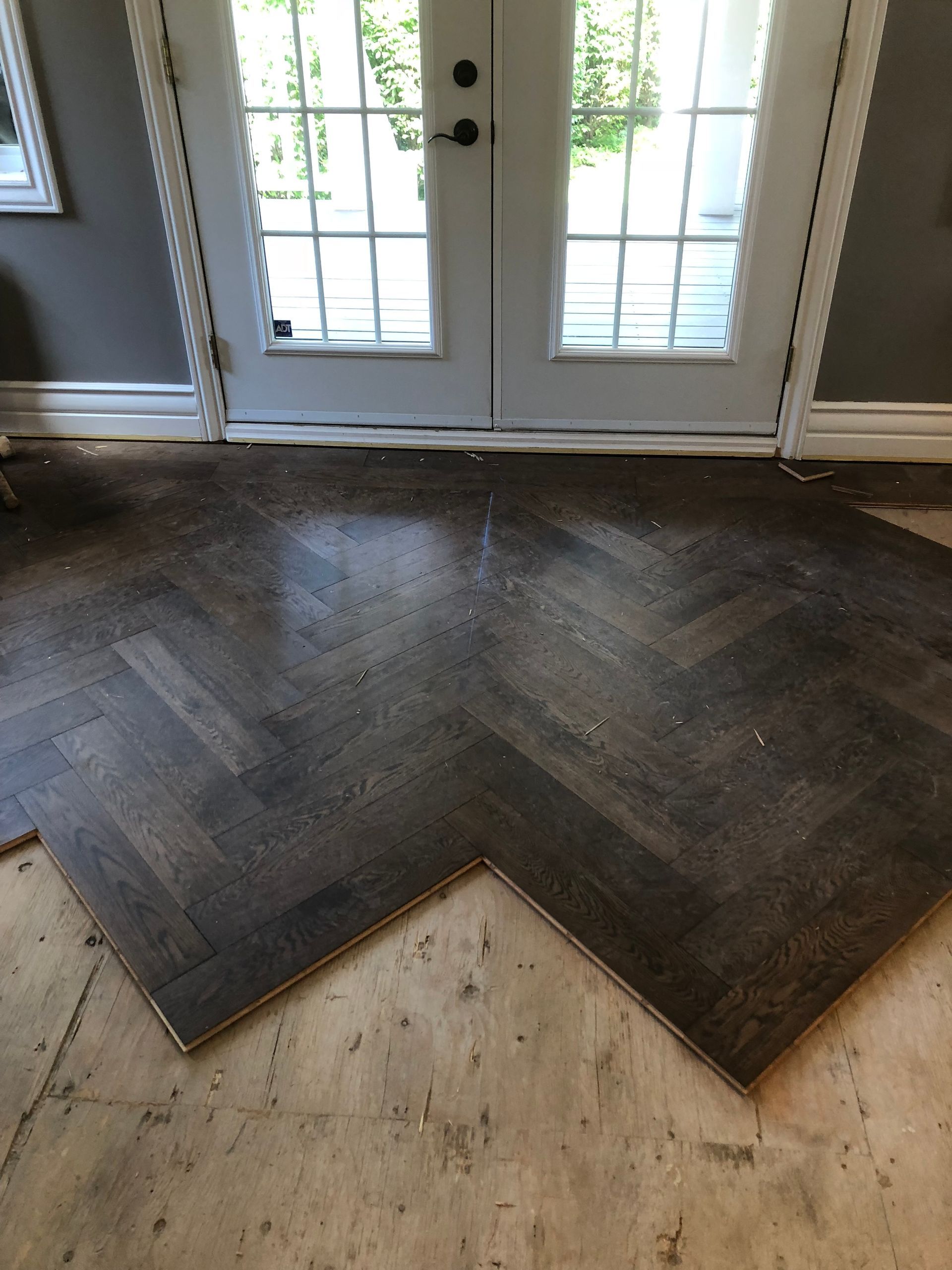 Un revêtement de sol foncé à chevrons, partiellement installé près des portes-fenêtres, repose sur un sous-plancher apparent.