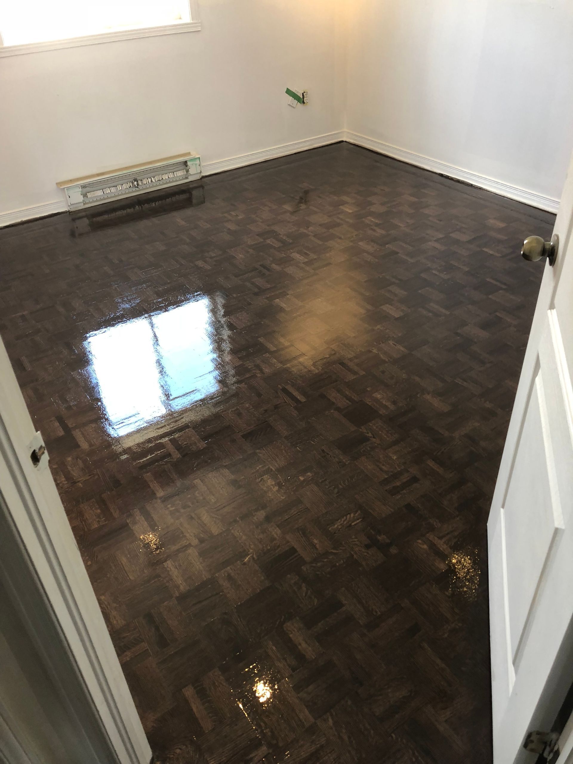 Vue d'une pièce avec parquet foncé, murs gris et moulures blanches ; du ruban adhésif vert souligne les plinthes.