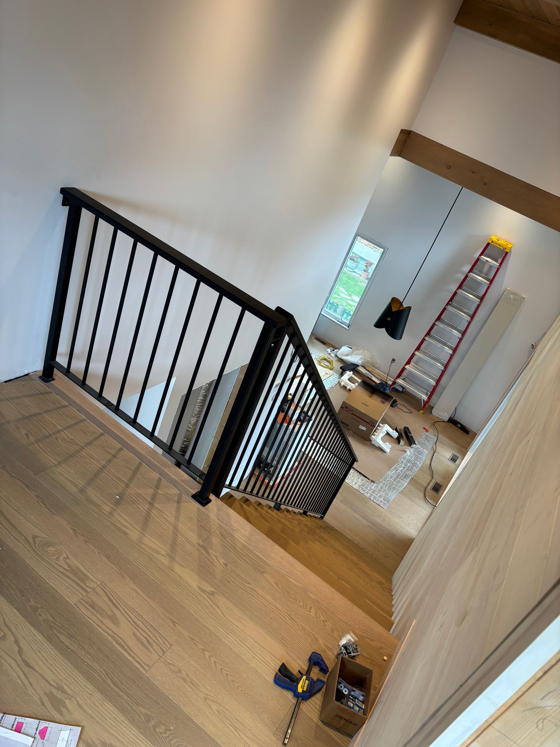 Escalier avec rampe noire et marches en bois, menant à une pièce en construction avec une échelle et des outils éparpillés.
