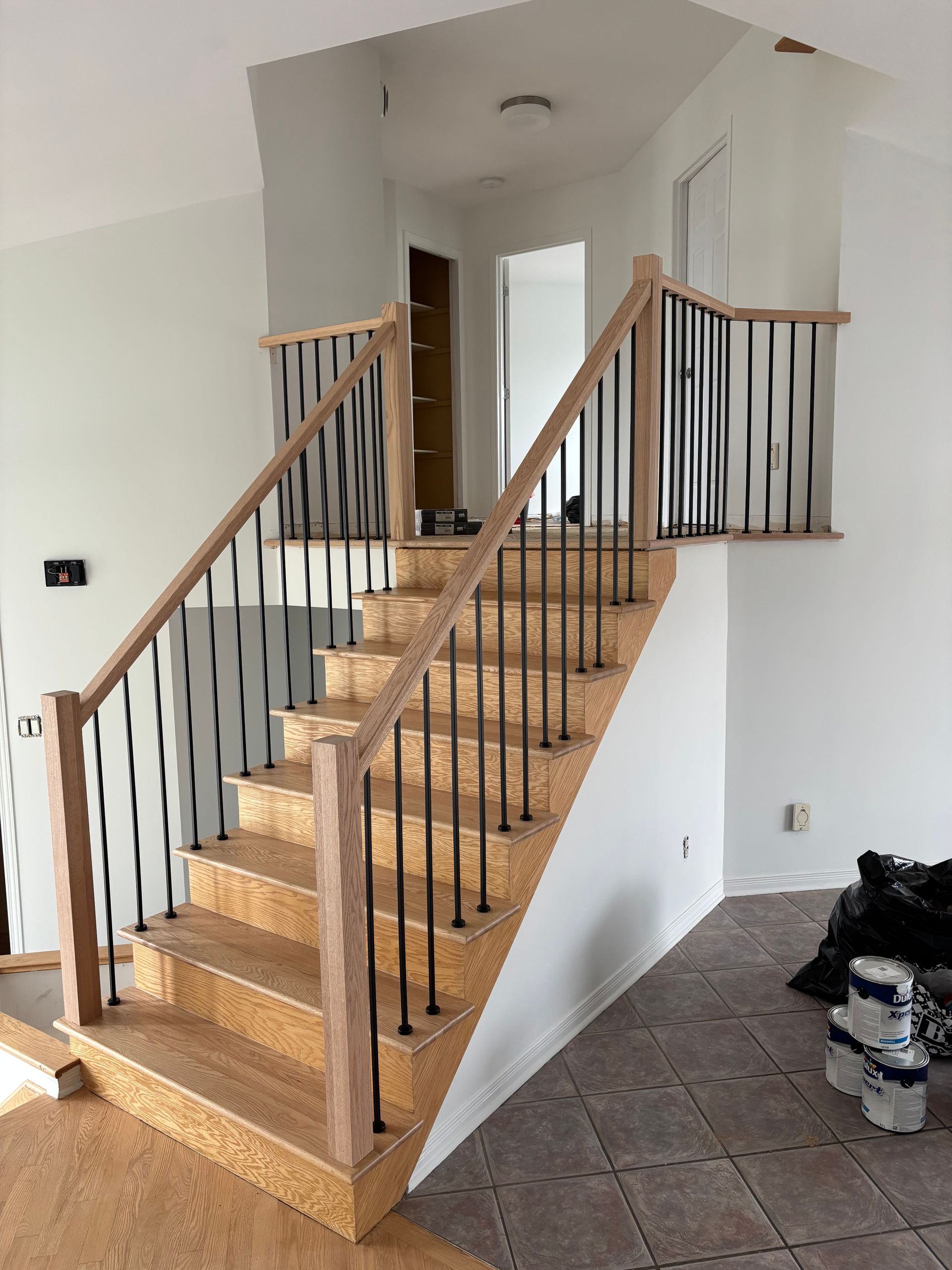 Escalier en bois avec des broches en métal noir, des rampes en bois clair et des murs neutres.