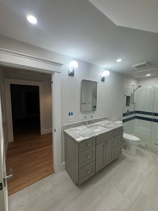 Modern bathroom with gray vanity, marble countertop, mirror, wall lights, and striped shower curtain.