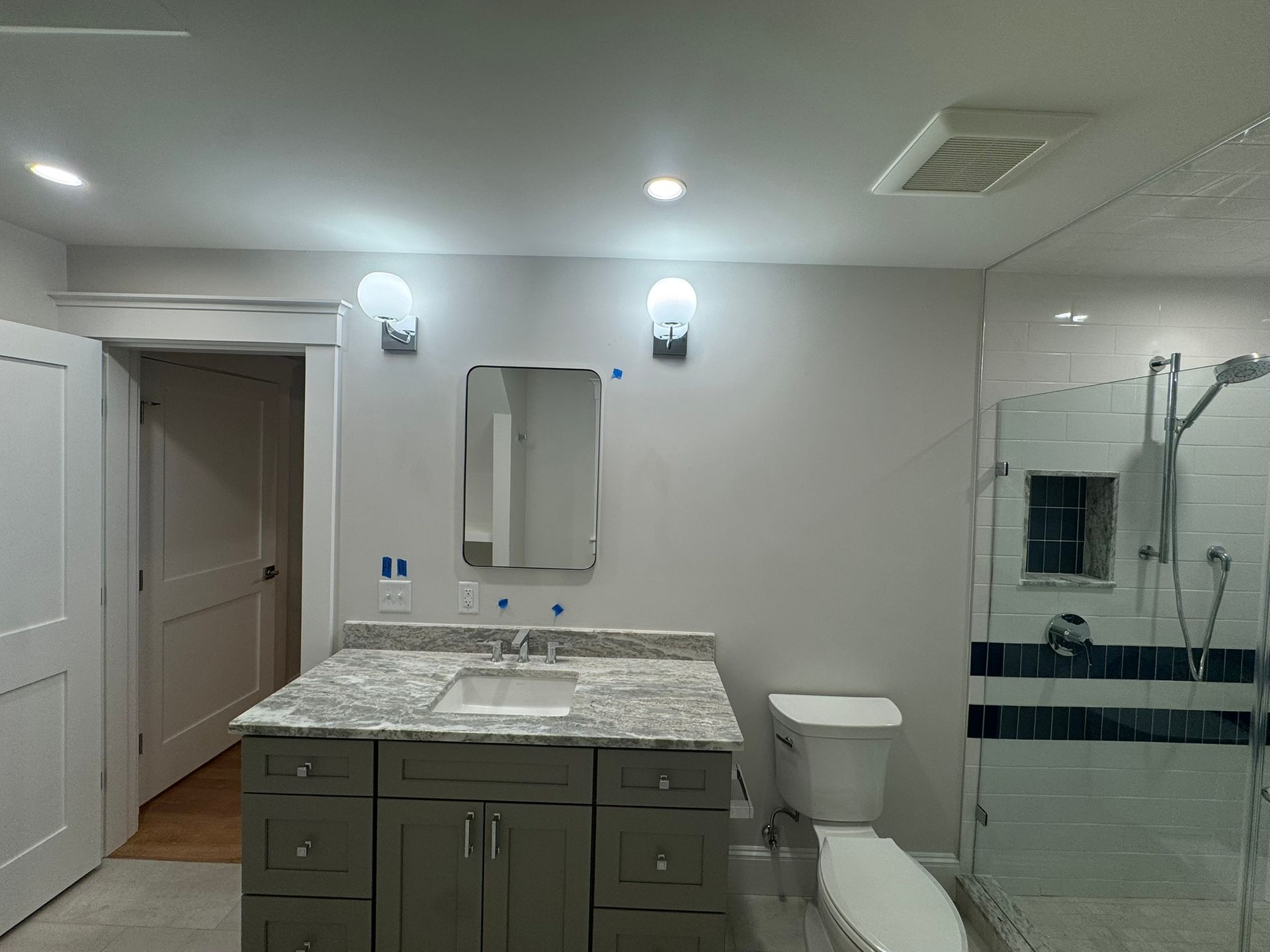 Modern bathroom with gray vanity, granite countertop, mirror, toilet, and glass shower enclosure