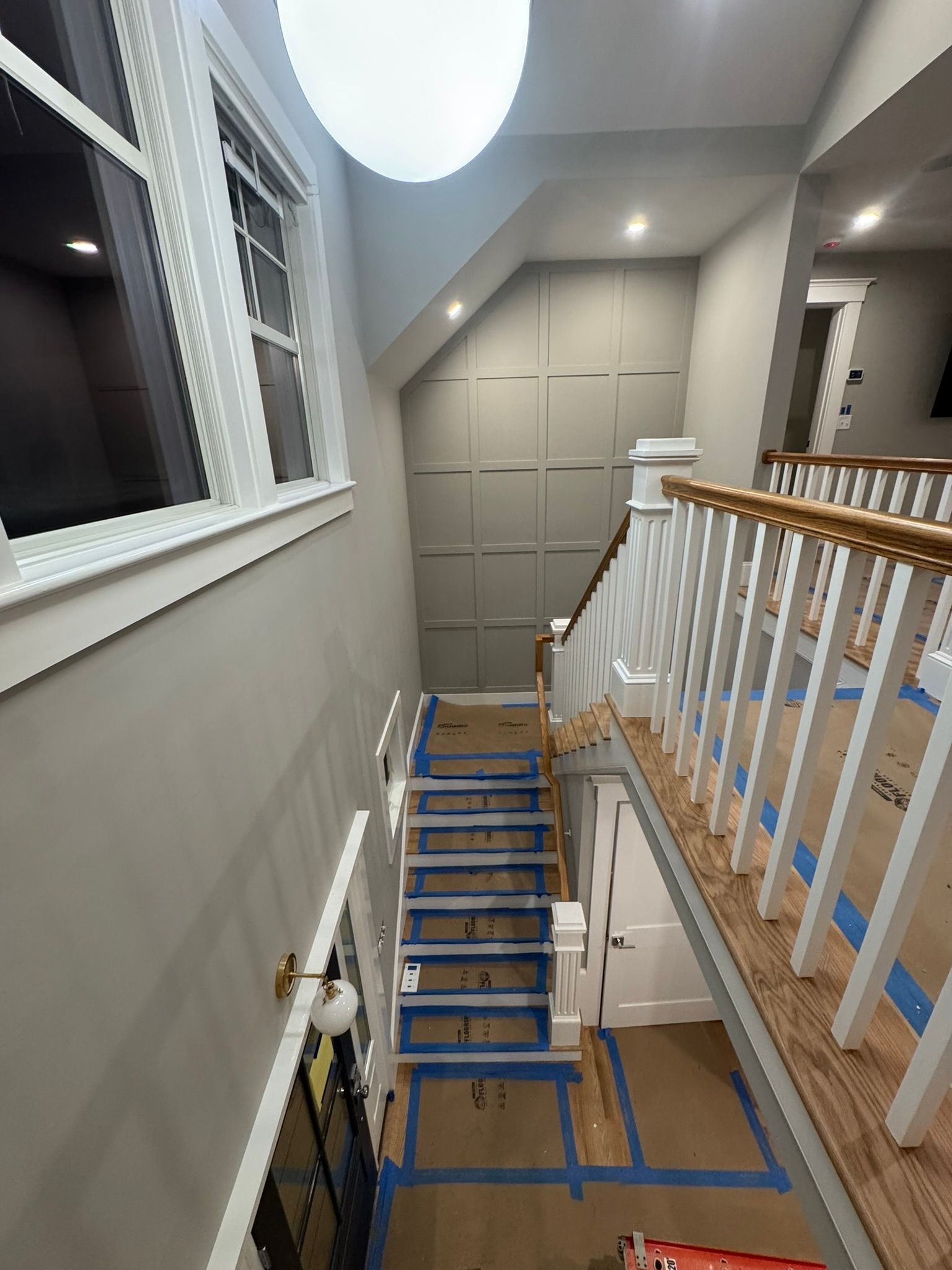 Hallway stair landing with taped-off steps, white banister, and closed cabinet doors at the top