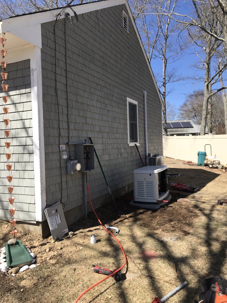 Side of a gray house with outdoor HVAC unit, utility meter, and red hoses on a dirt yard.