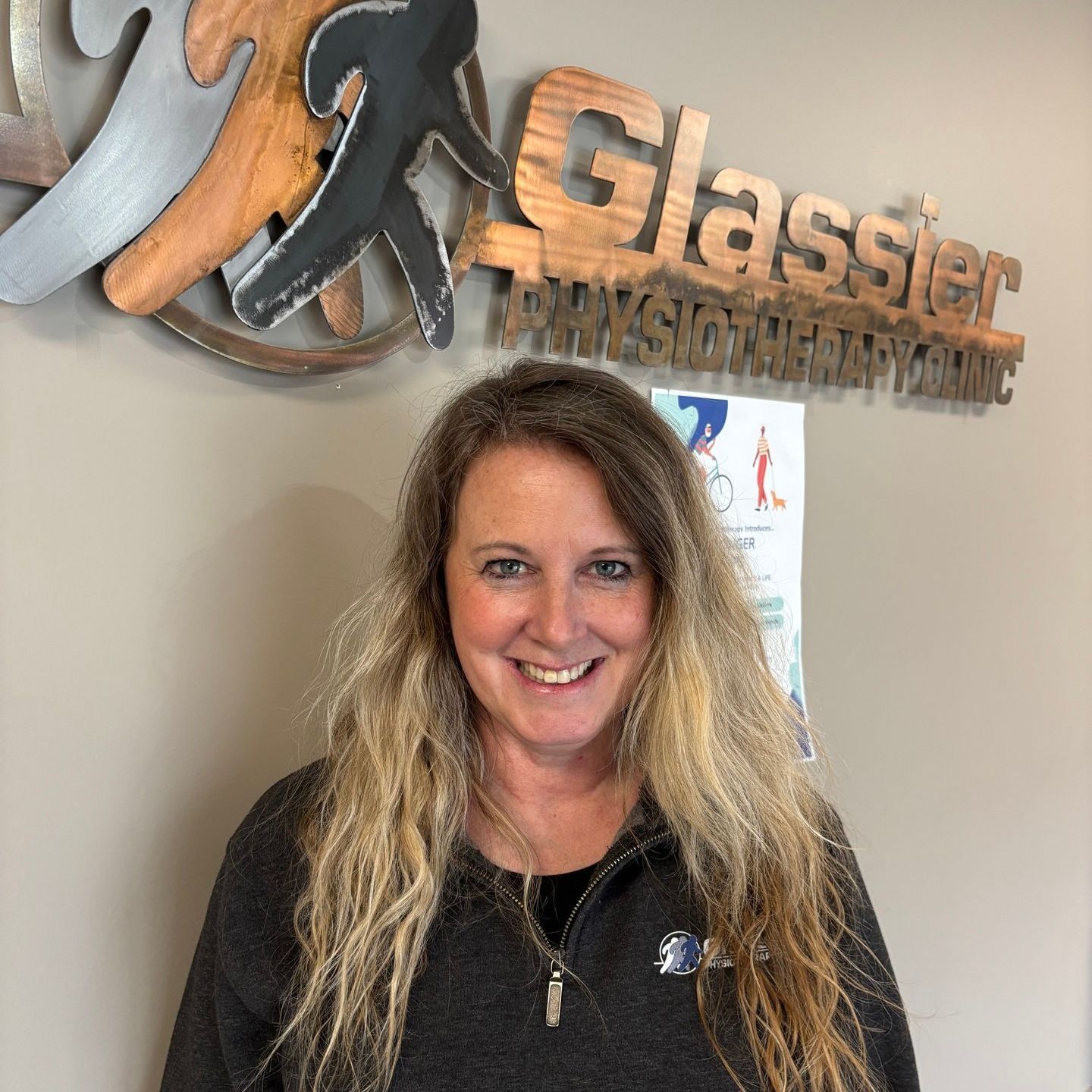 A woman is smiling in front of a glassier sign.