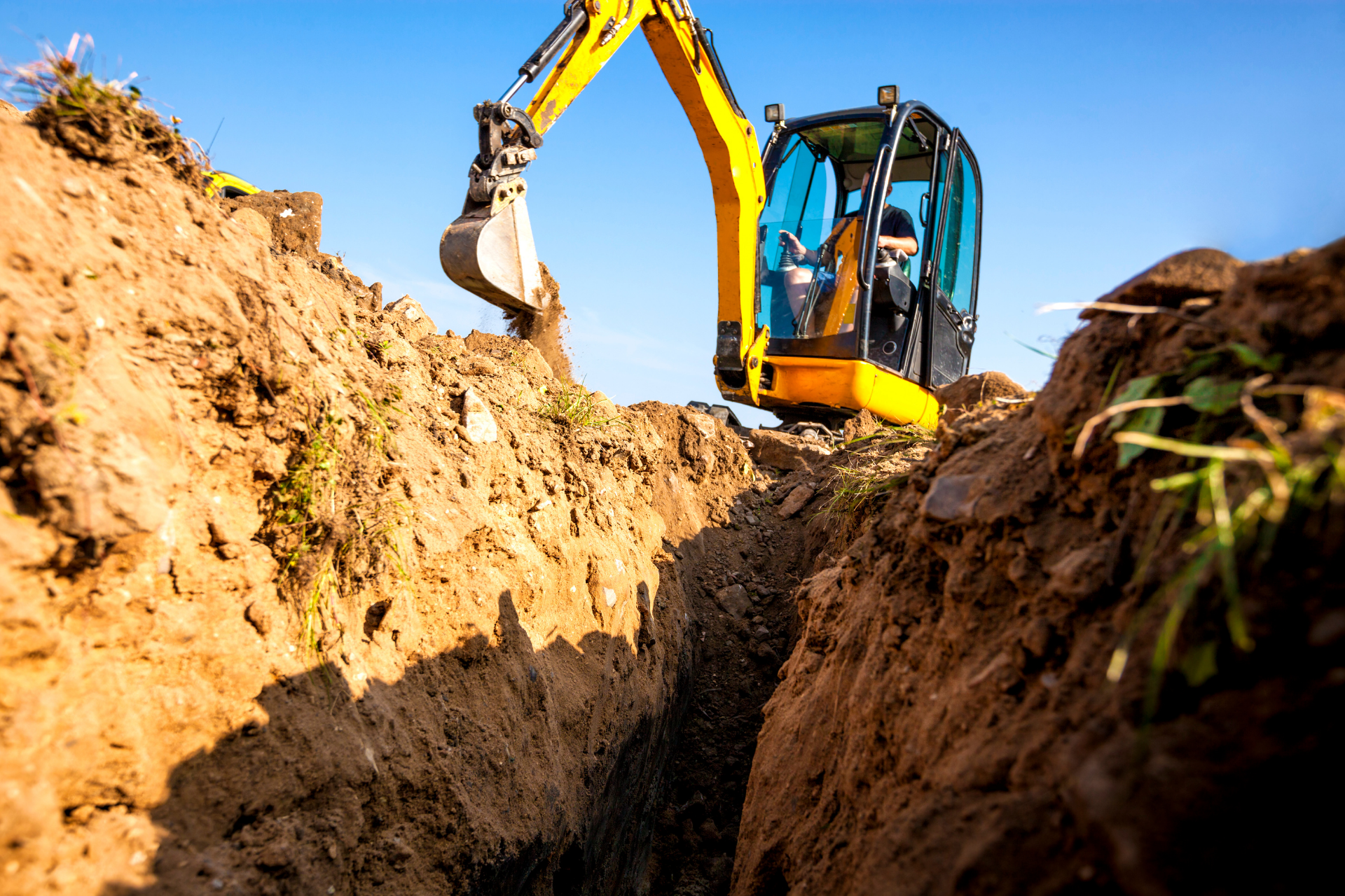 A yellow excavator is digging a trench in the dirt.