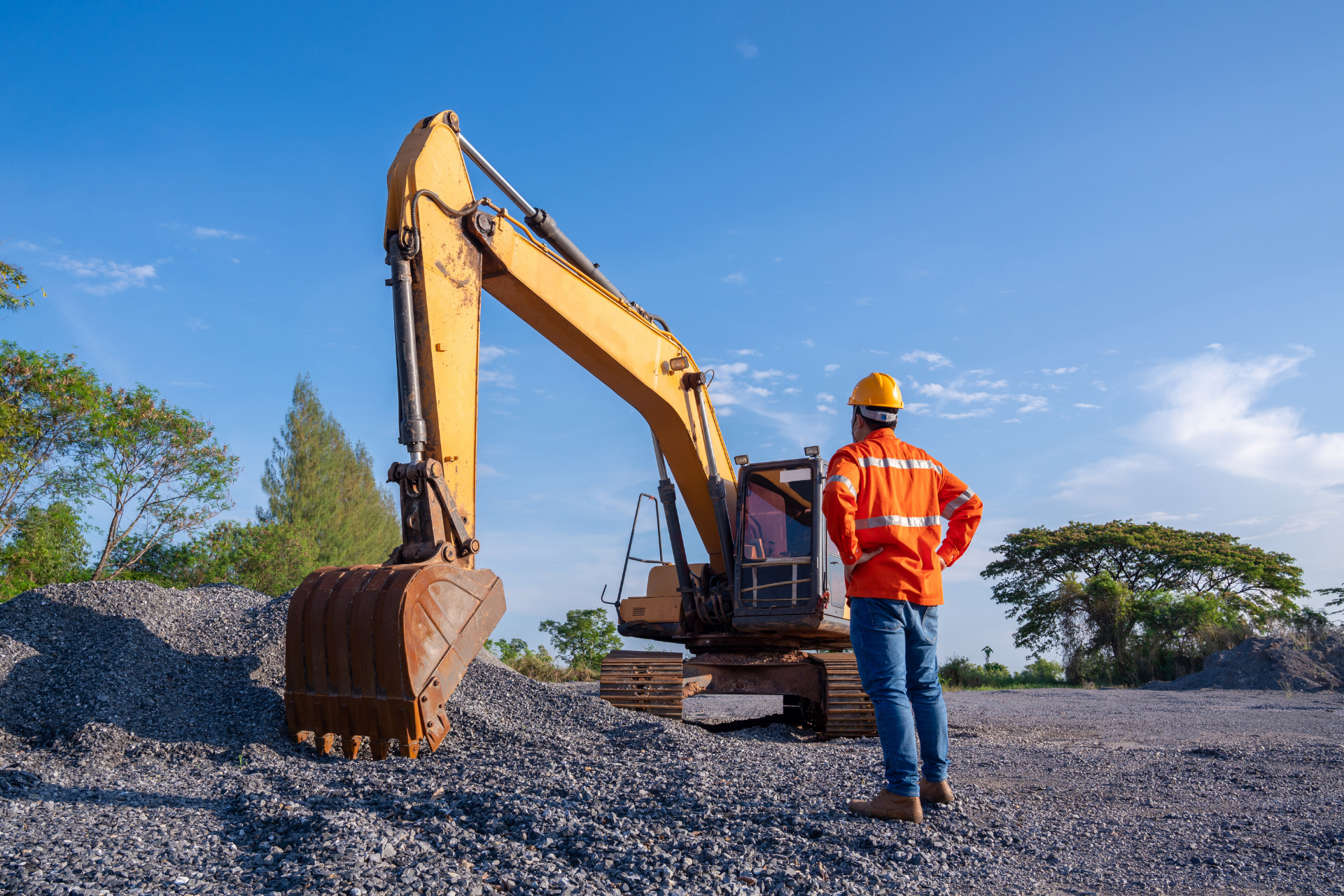 A construction worker is standing in front of an excavator at a construction site.
