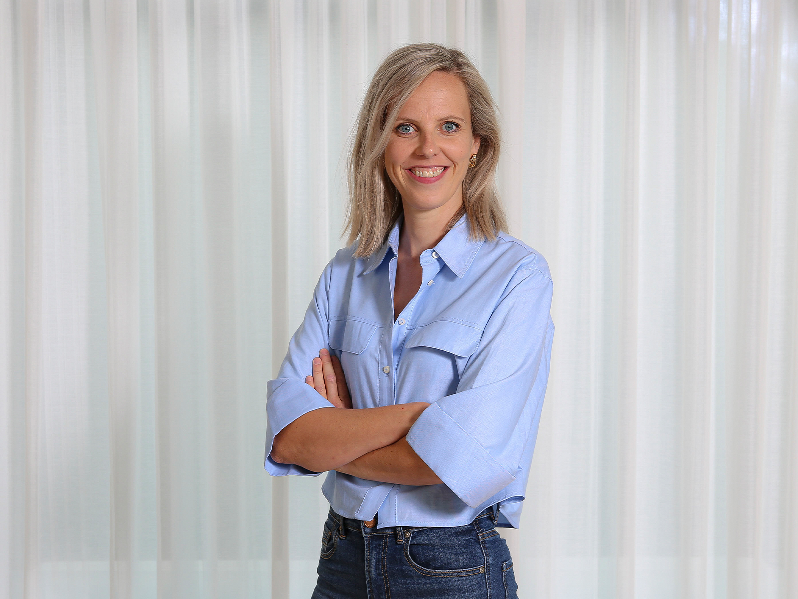 Vrouw die met gekruiste armen lachend in de camera kijkt