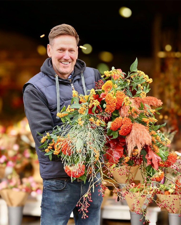 Man die een groot bloemstuk vasthoudt in een bloemenwinkel