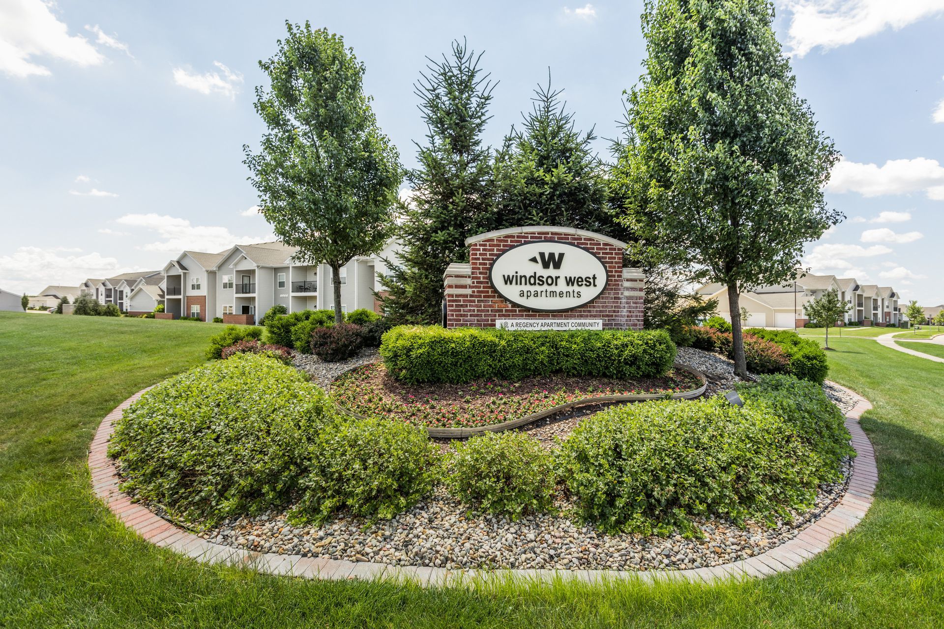 a sign for windsor west apartments is surrounded by trees and bushes
