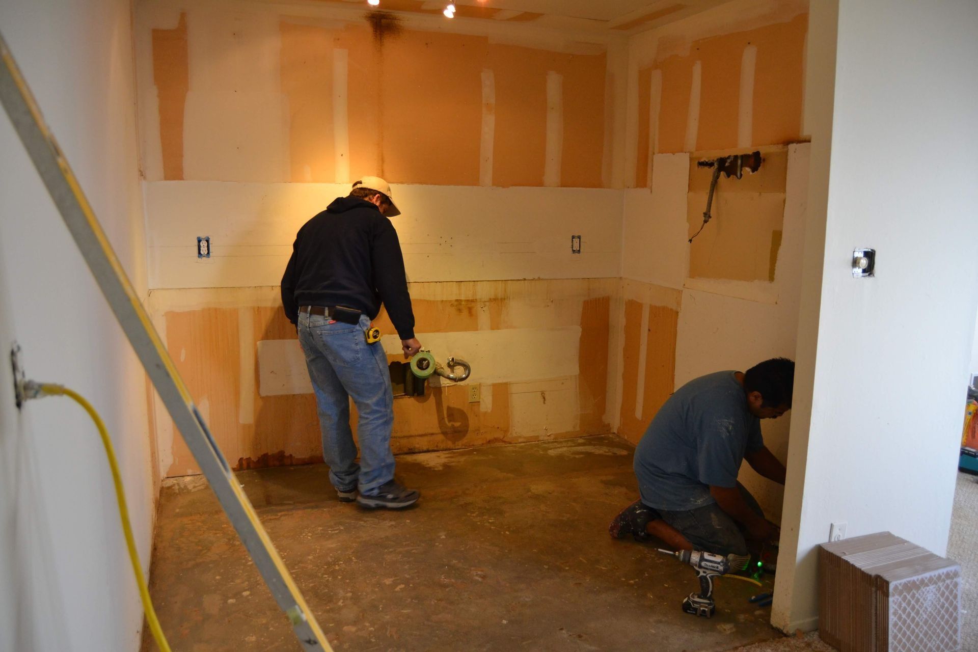 Two men are working on a kitchen in a room.