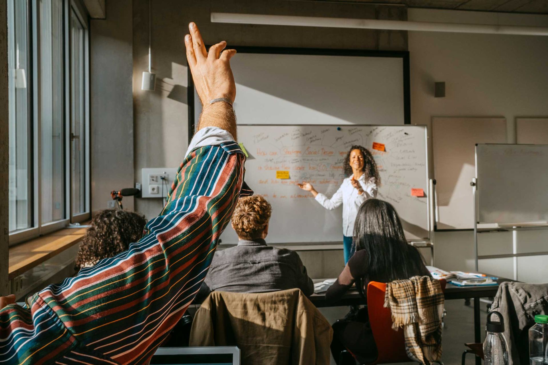 A man is raising his hand in a classroom to answer a question.