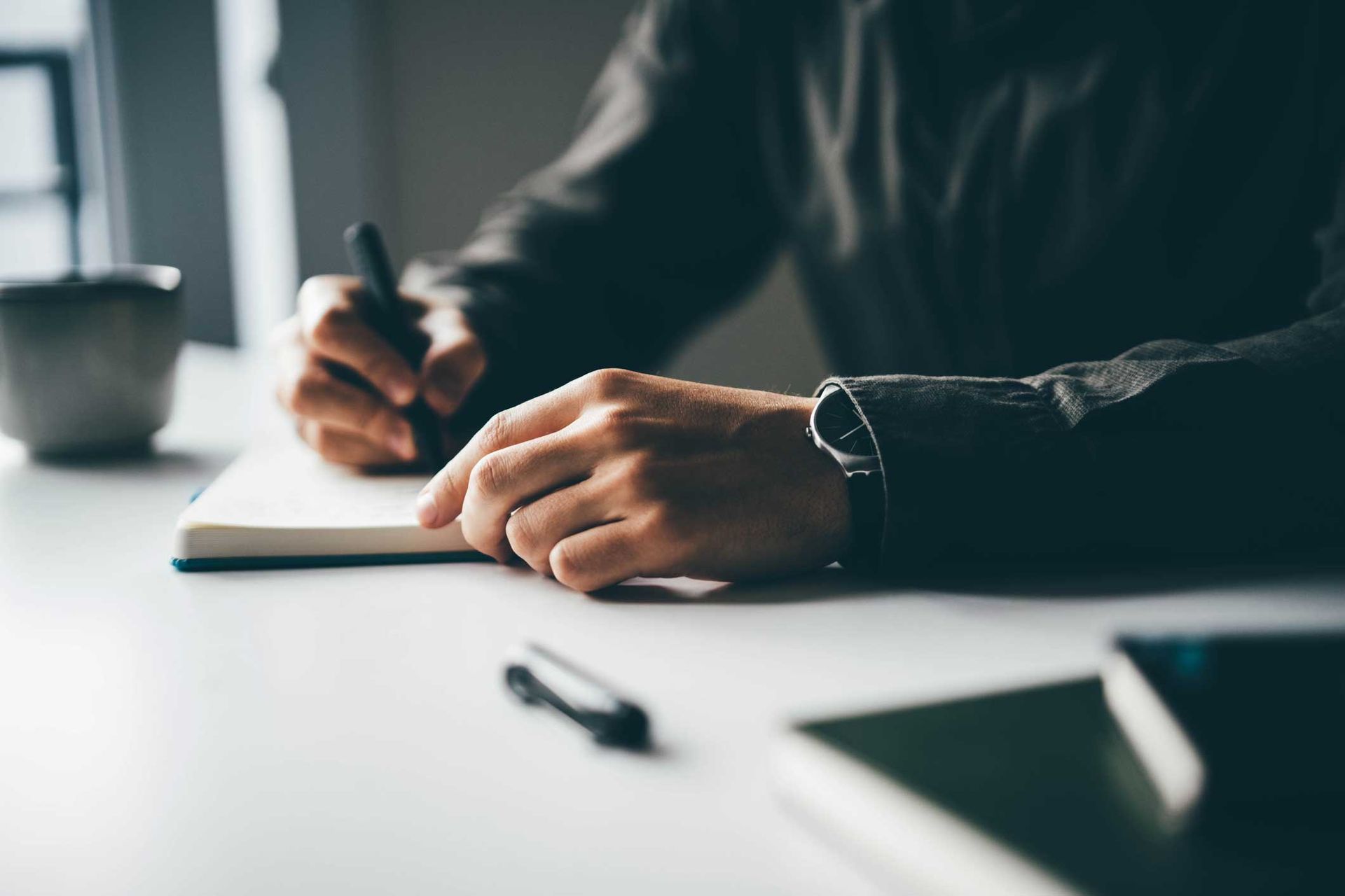A man is sitting at a desk writing in a notebook.