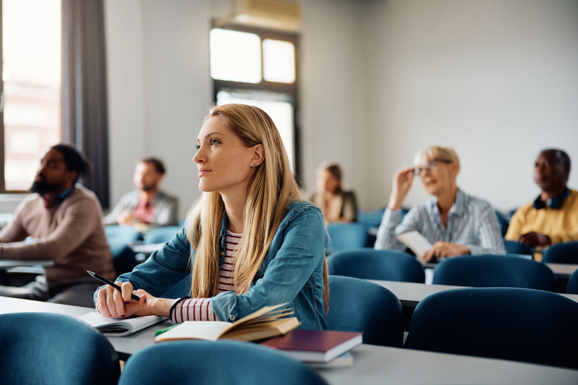 A woman is sitting at a desk in a classroom with other students.