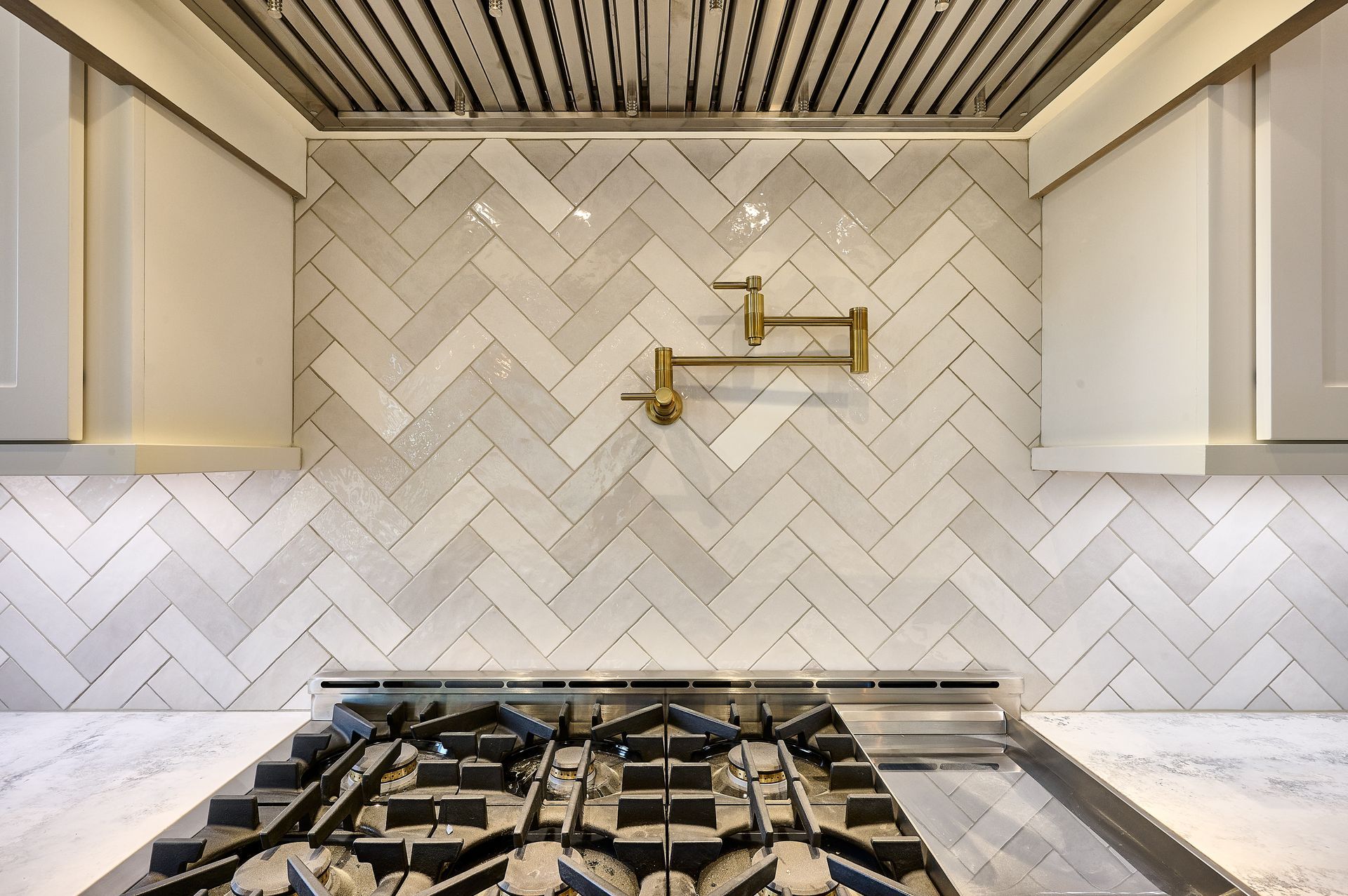 Kitchen backsplash with herringbone tile, range, and gold pot filler.
