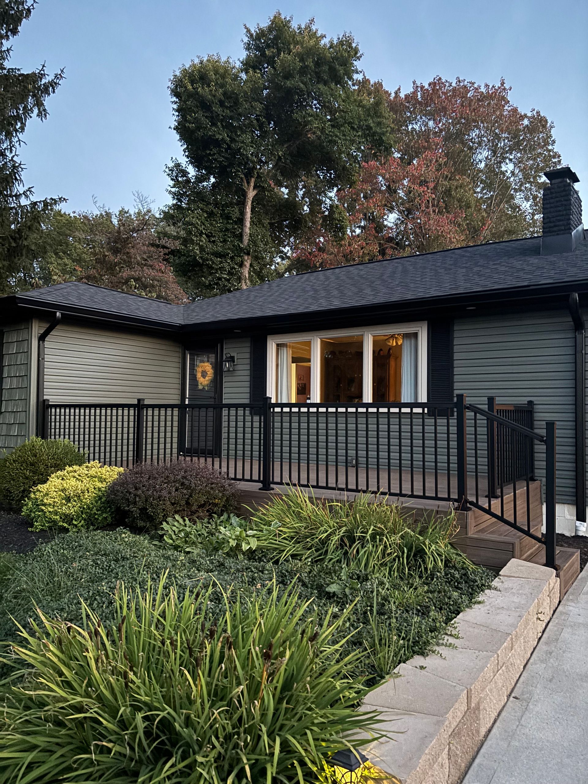 Green house with black trim, a black railing, and lush landscaping.