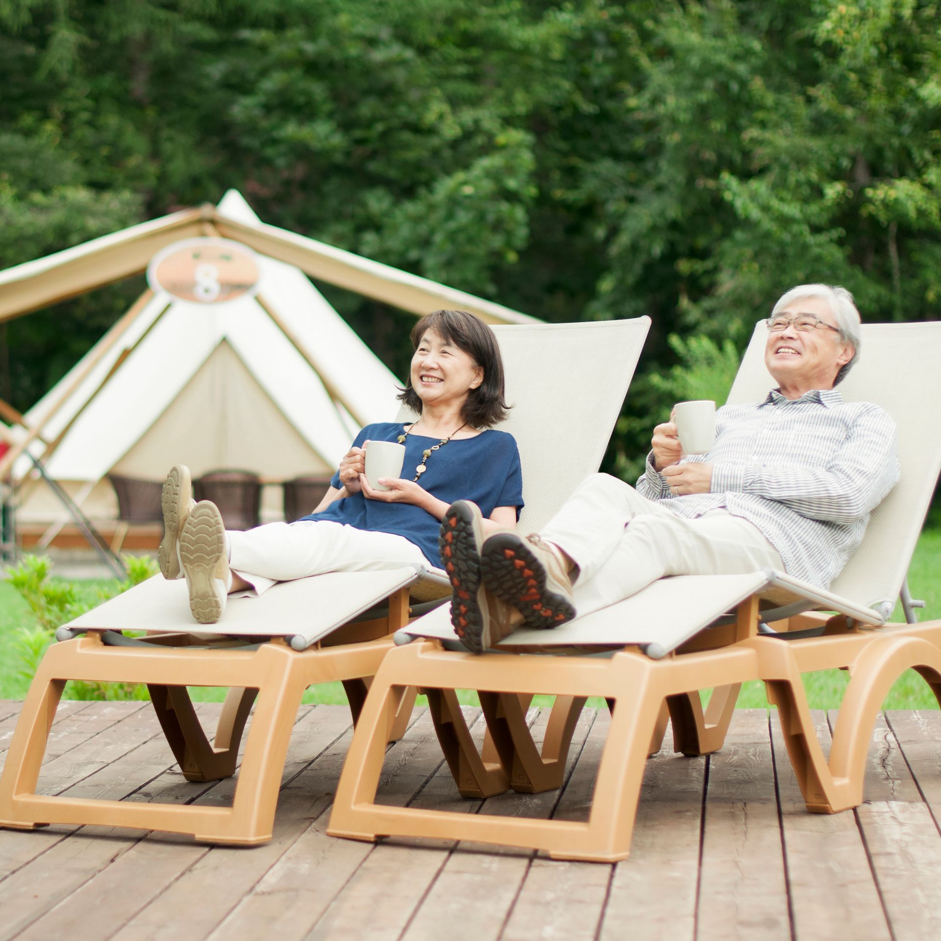 Two people relaxing on reclining chairs outside a modern caravan at a campsite.