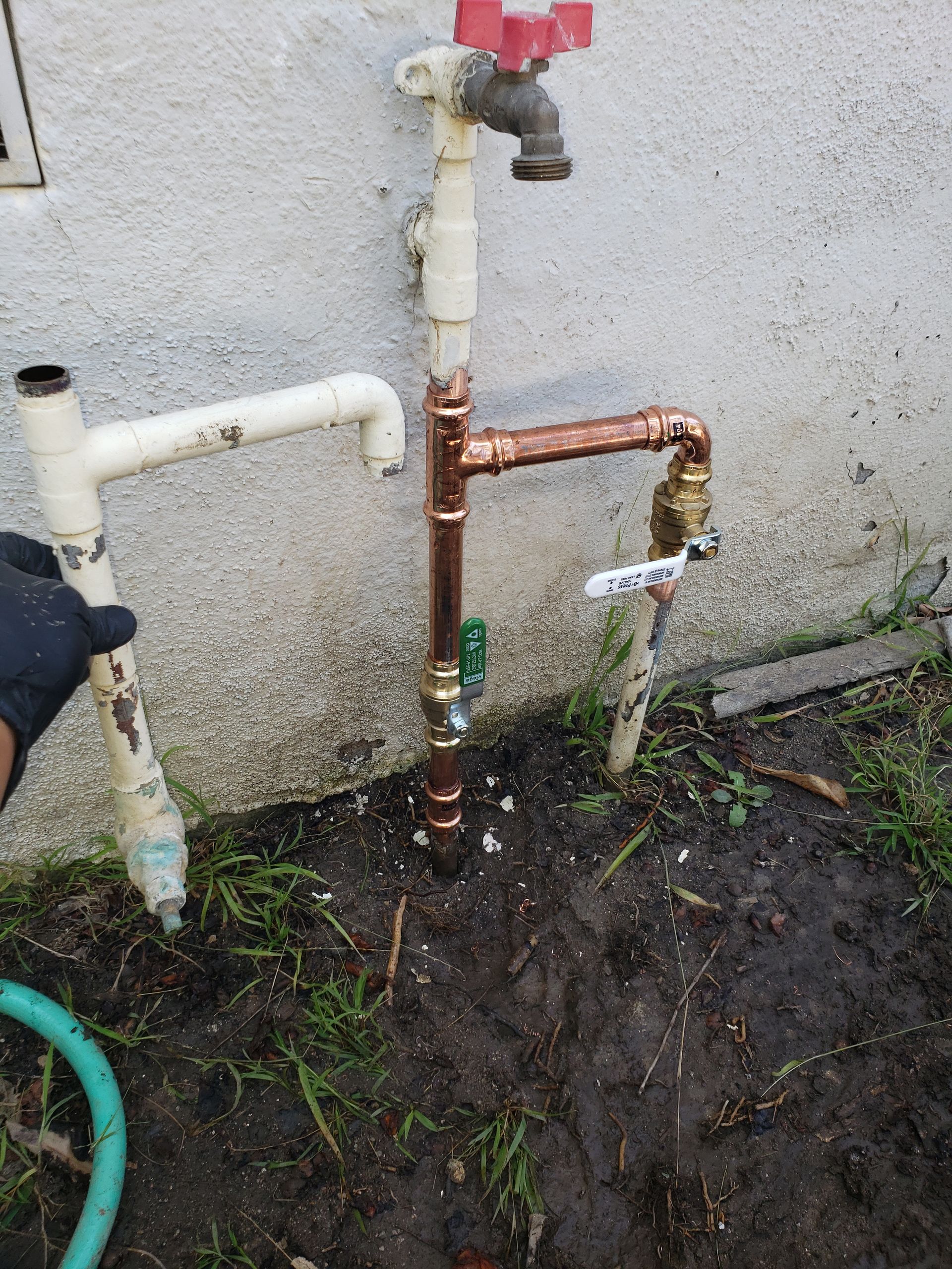 A person is fixing a faucet on the side of a building.