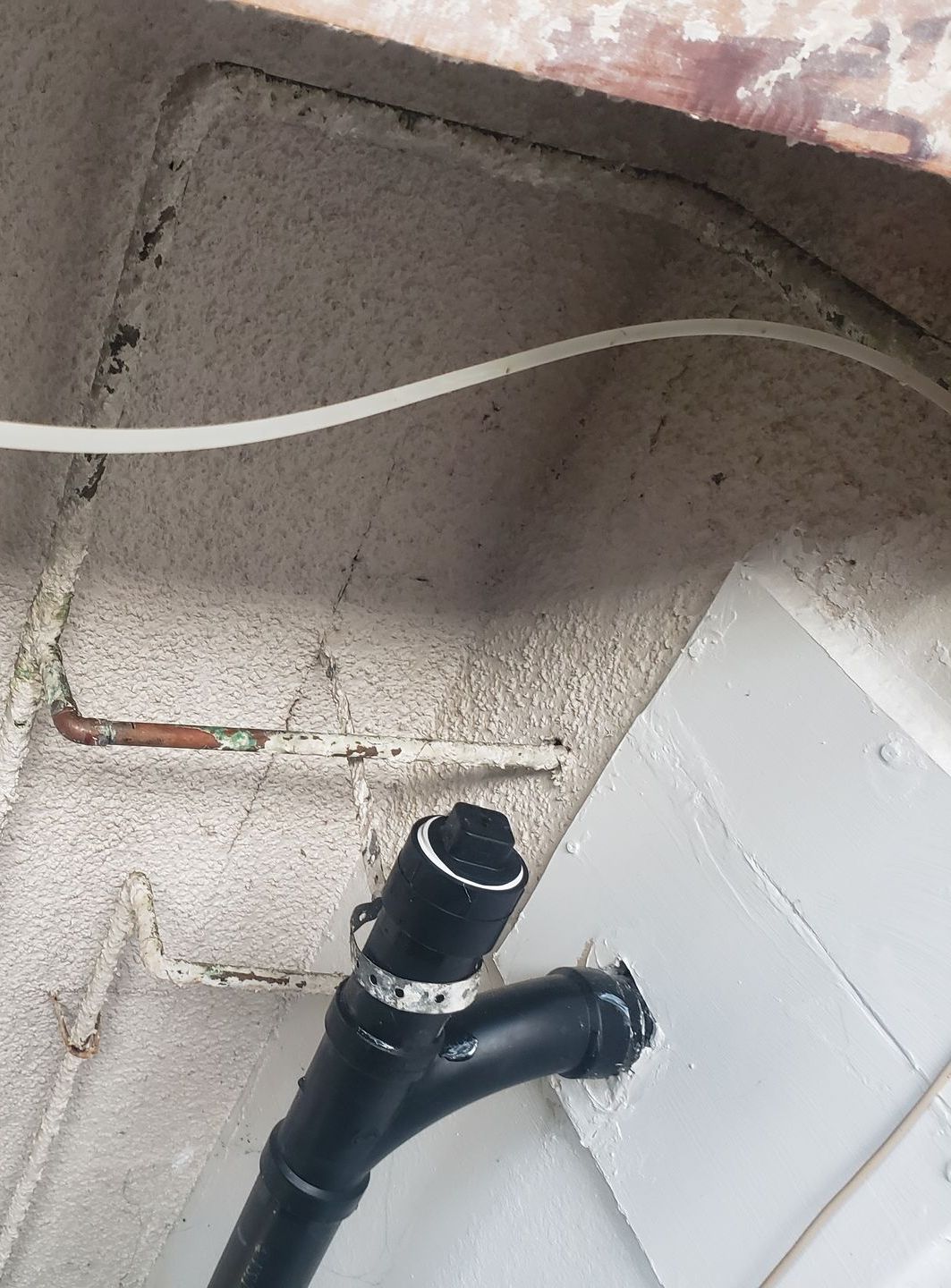 A black pipe is connected to a white wire on a brick wall.