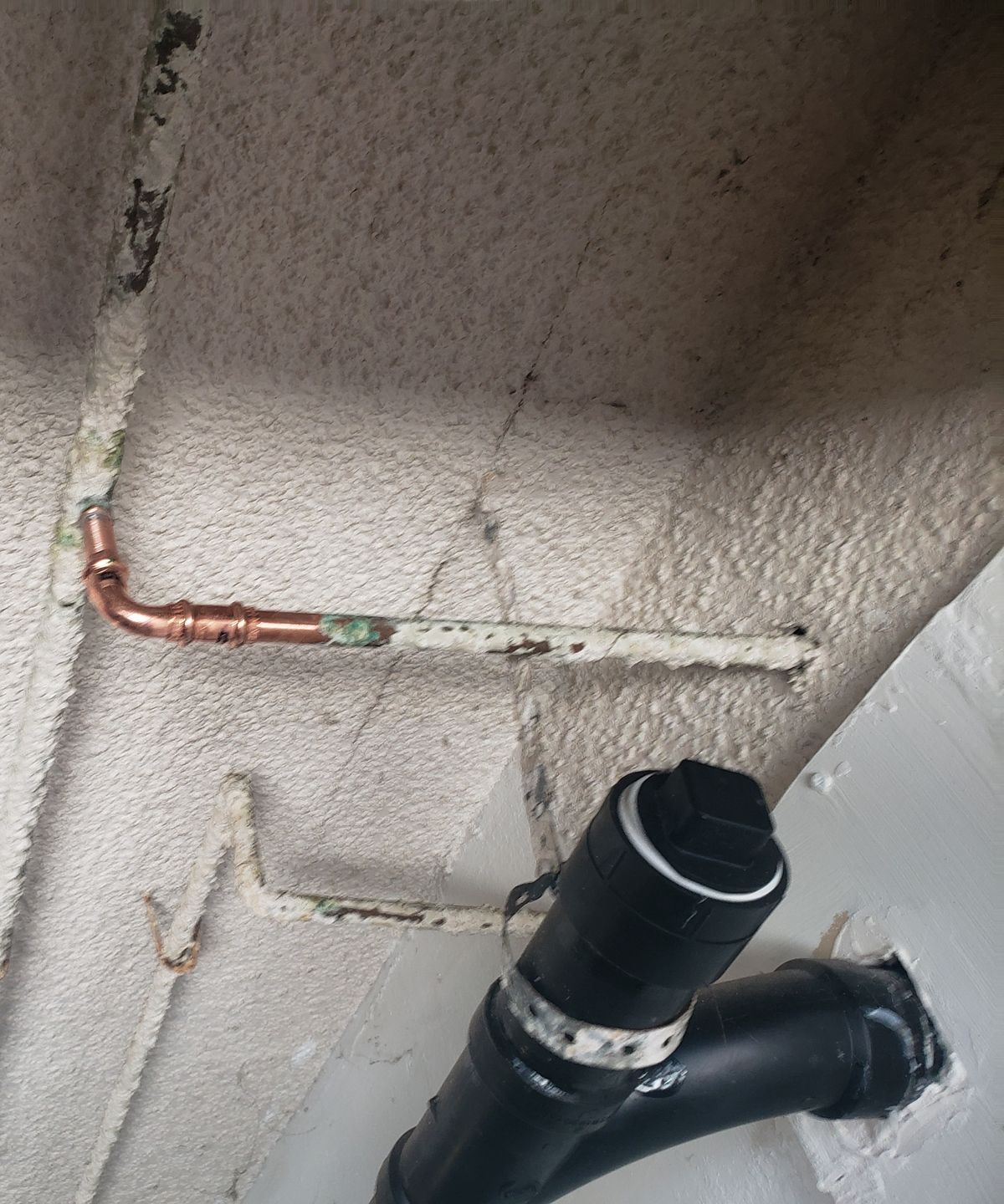 A copper pipe is connected to a black pipe on a wall.