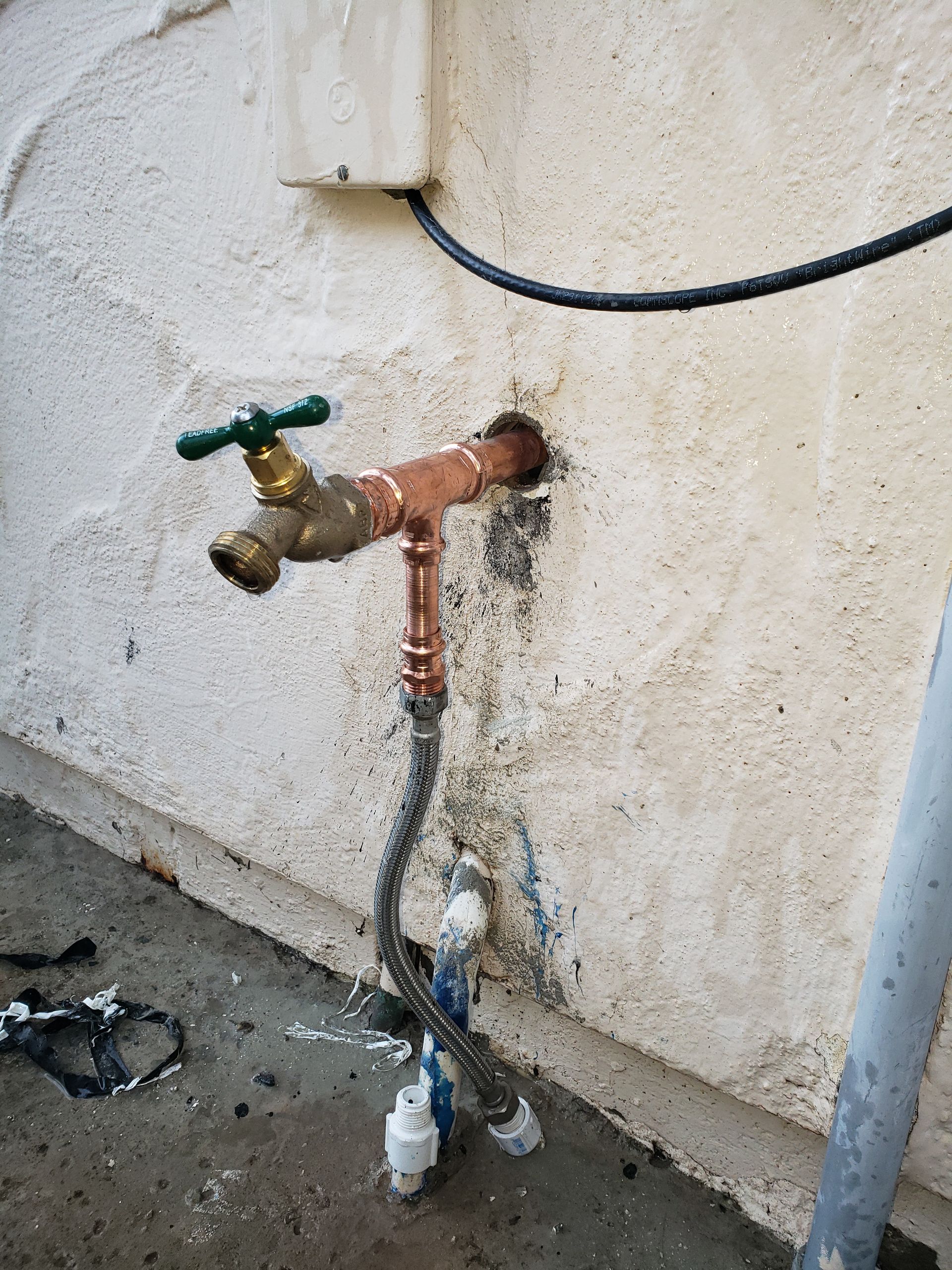 A faucet with a green handle is attached to a wall.