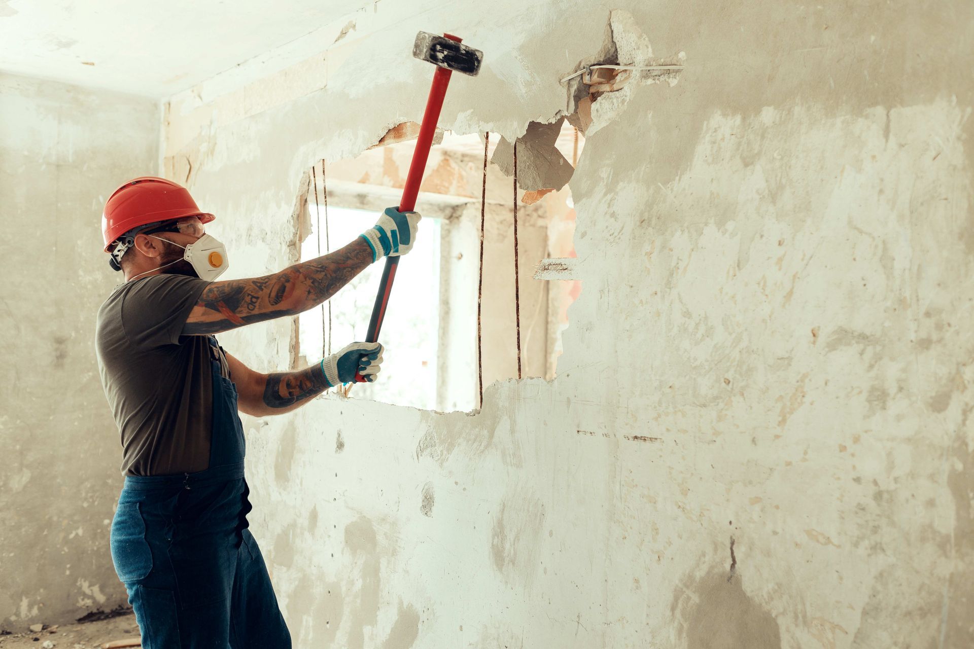 Builder with a hammer in his hands breaks the cement wall.