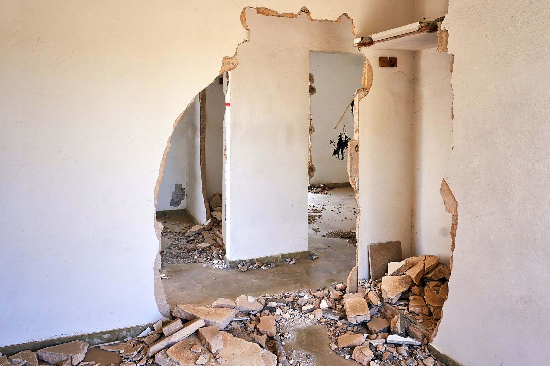 Room with a large hole in the wall and debris scattered on the floor.