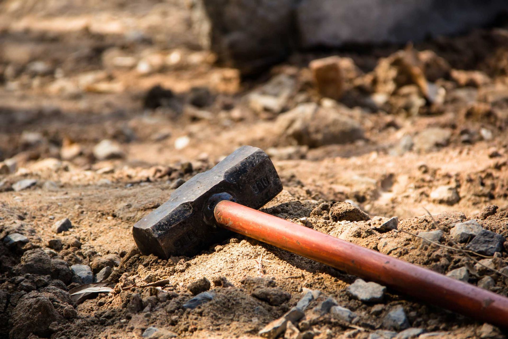 Red-handled sledgehammer on rocky dirt ground at construction site for demolition or building work. Red-handled sledgehammer on rocky dirt ground at construction site for demolition or building work.
