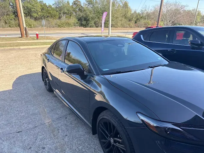 Black Chevrolet Camaro in a garage, black wheels, yellow line on the floor, promotional banners on the wall.
