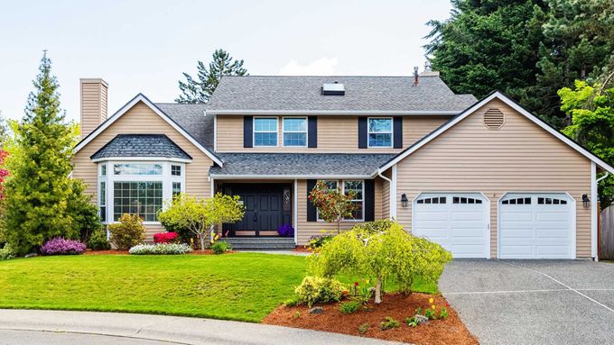 A large house with two garage doors and a lush green lawn.