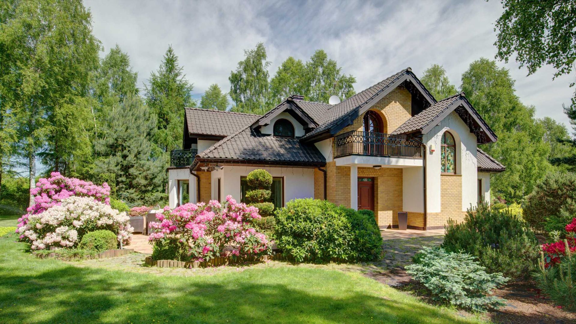 A large house with a lush green lawn and flowers in front of it.