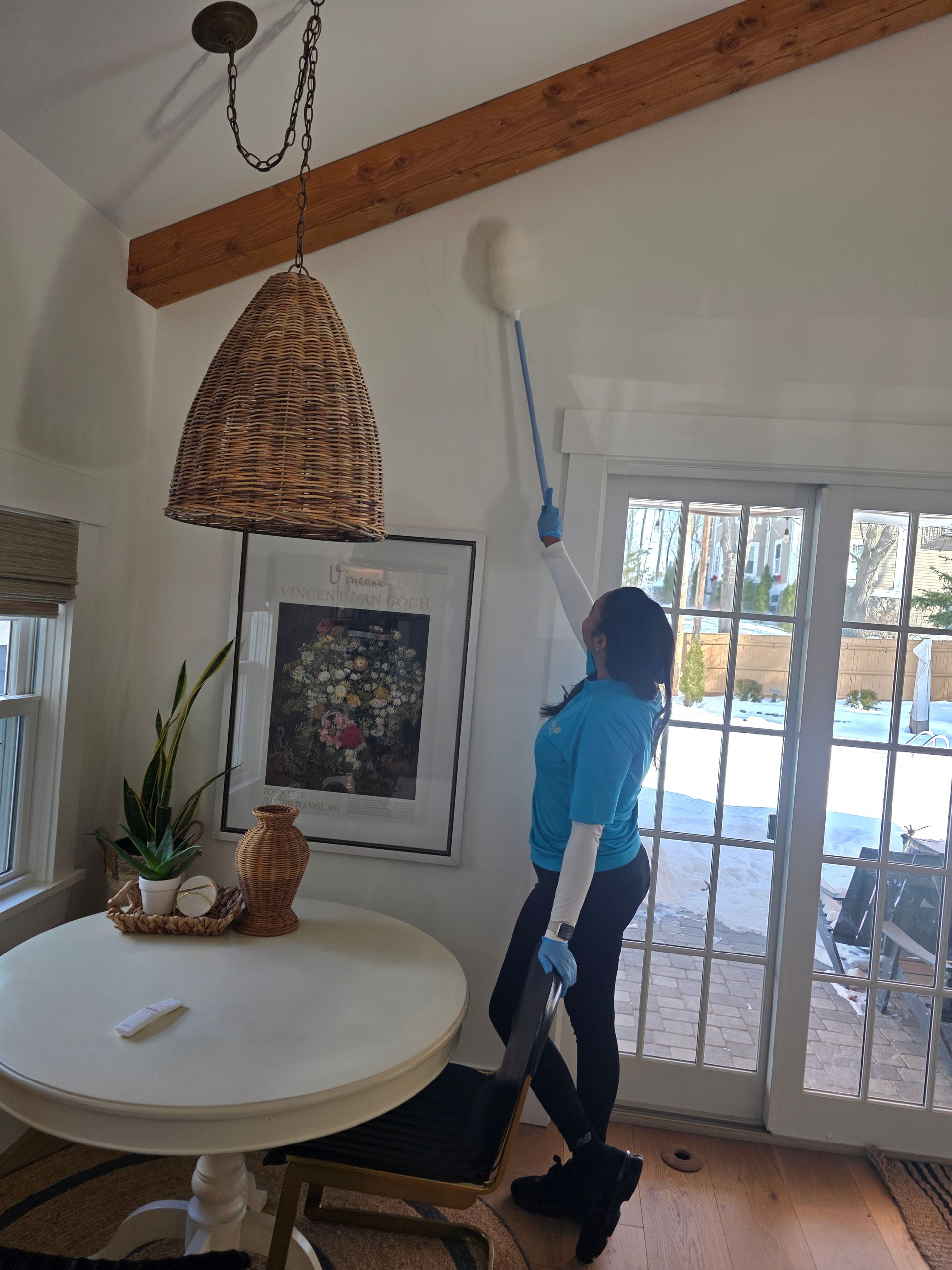 Person using a broom in a bright dining room with glass doors and a round table