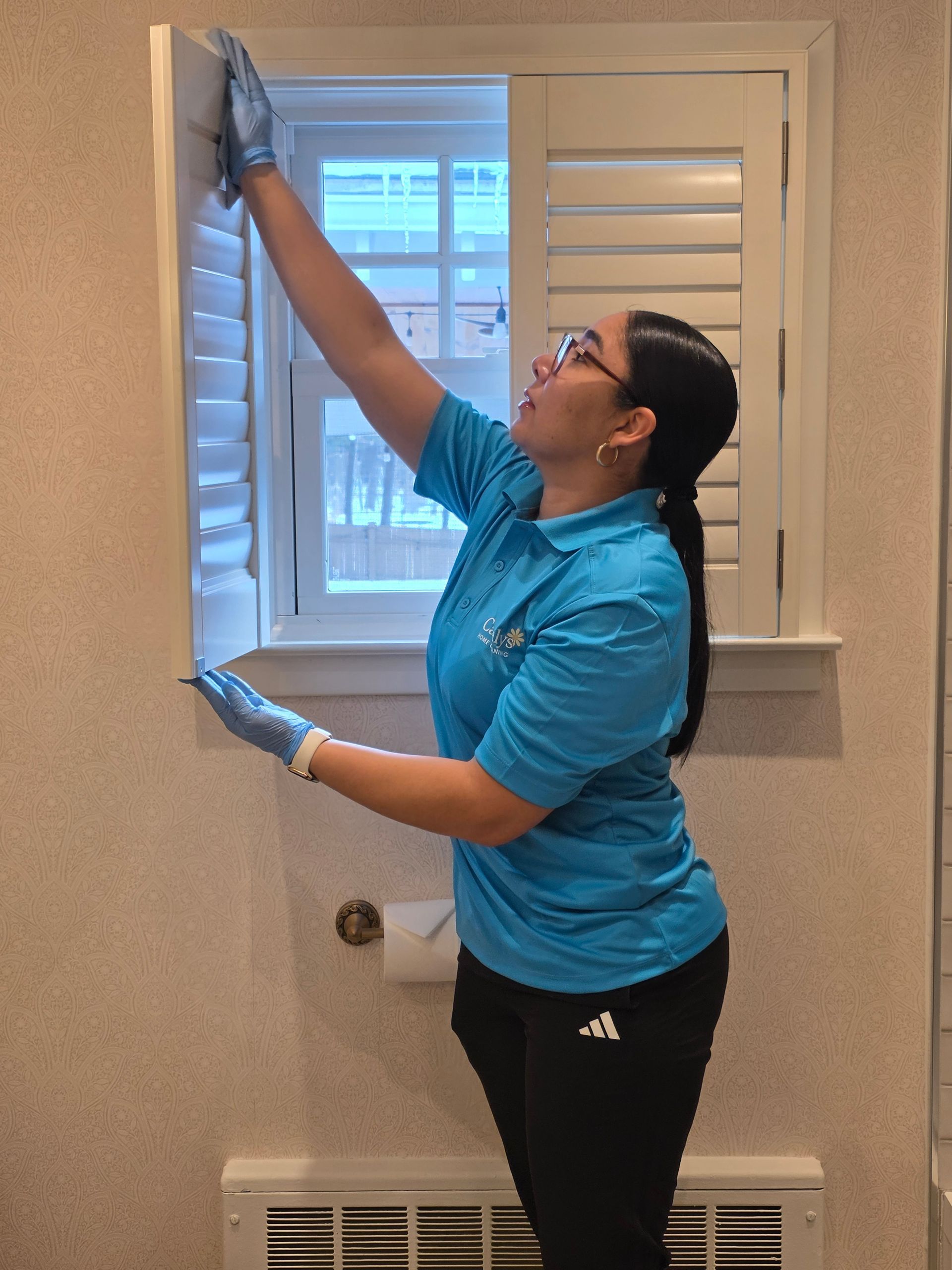 Person in blue shirt painting a window frame with a paintbrush and roller in a bathroom.